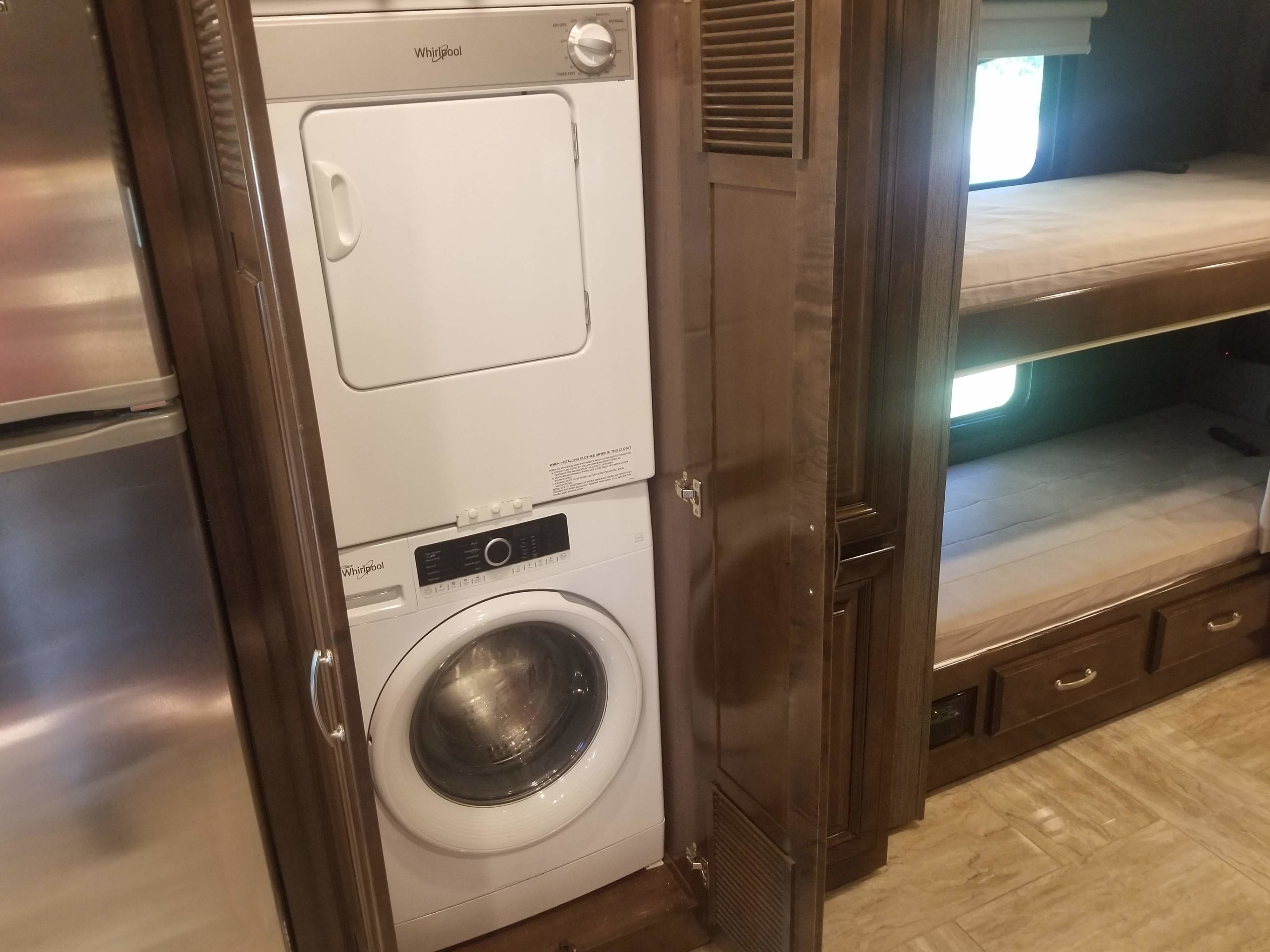 RV rental featuring a stacked Whirlpool washer/dryer, stainless steel refrigerator, and bunk beds in a wood-paneled interior.. Thor Aria 2020