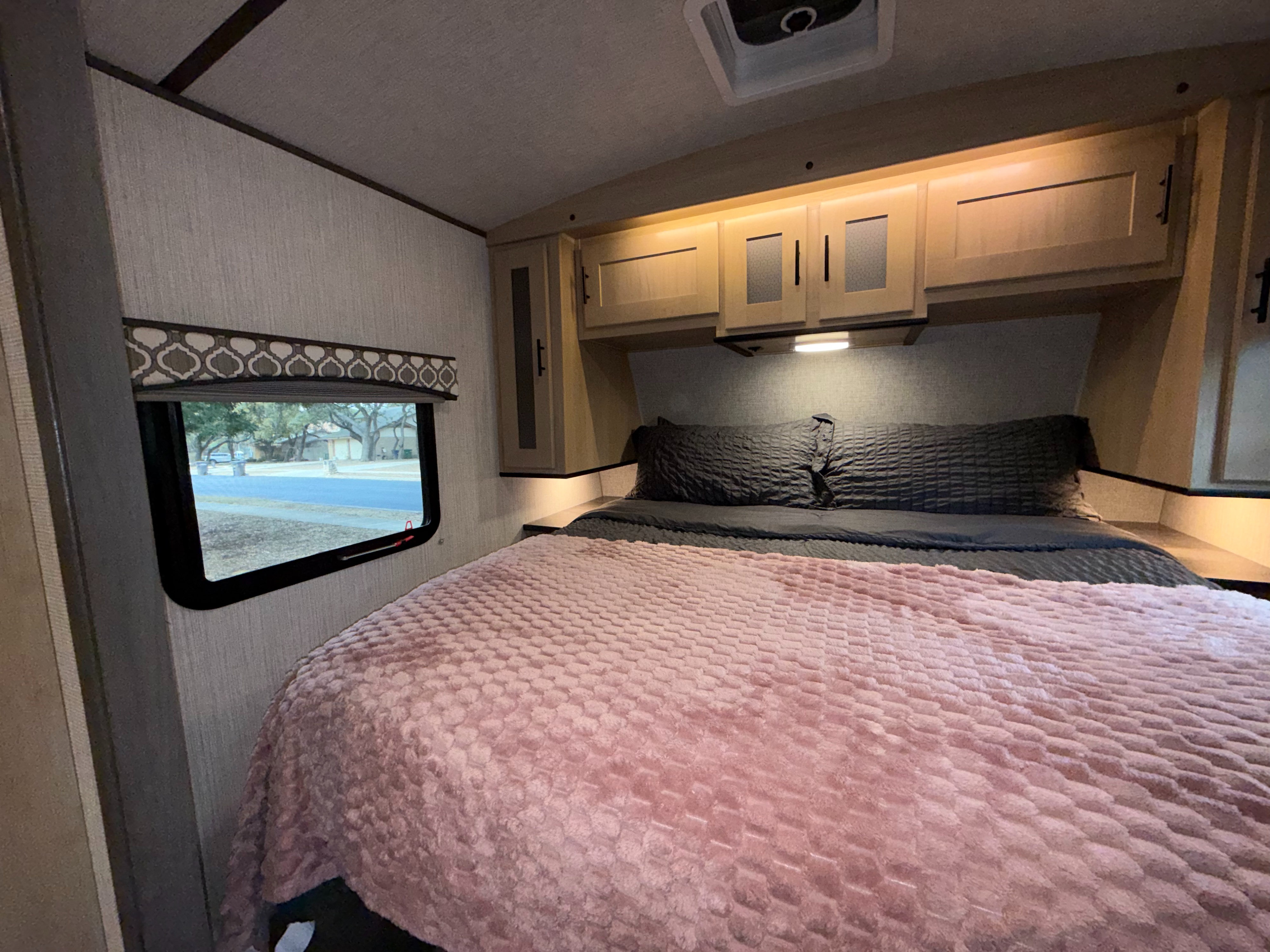 Cozy rv rental bedroom interior features light wood cabinets, a plush pink blanket, and a window with an outdoor view.. Cruiser RV Radiance Ultra Lite 2020