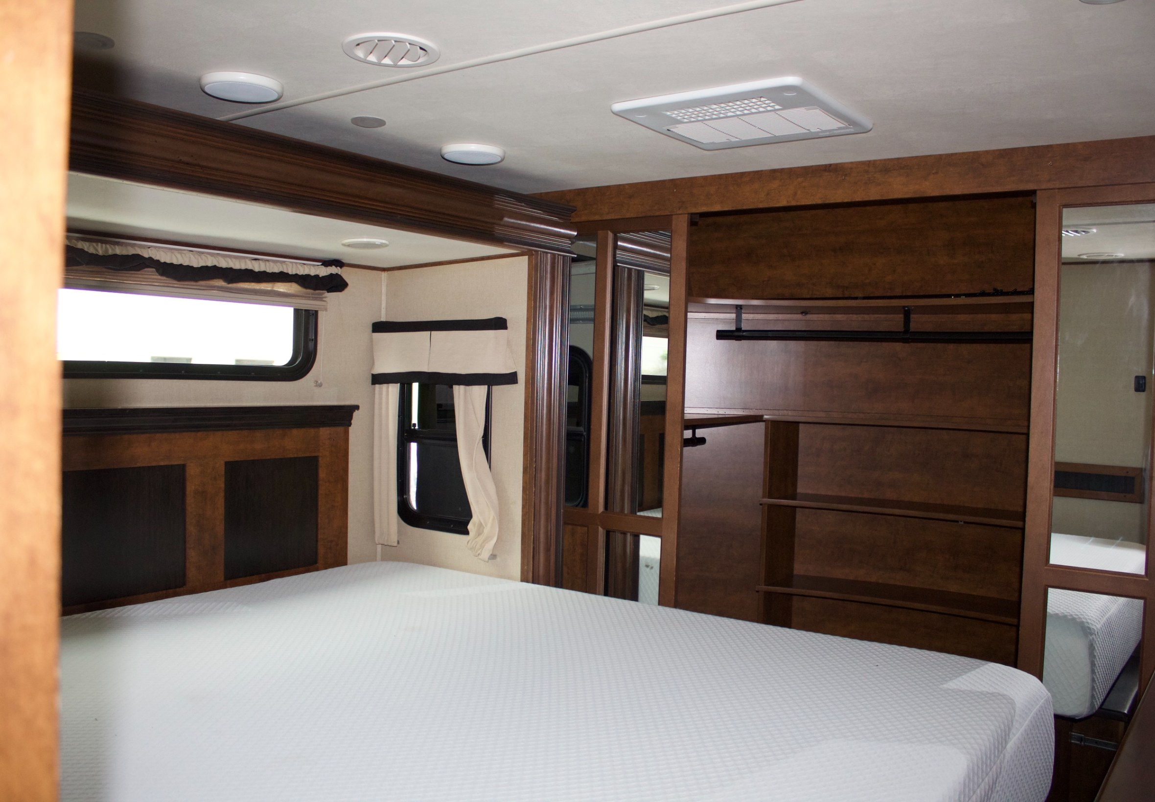 Explore the cozy bedroom of this RV rental, featuring a large white bed, windows, and dark wood cabinetry with a wardrobe.. Grand Design Solitude 2015