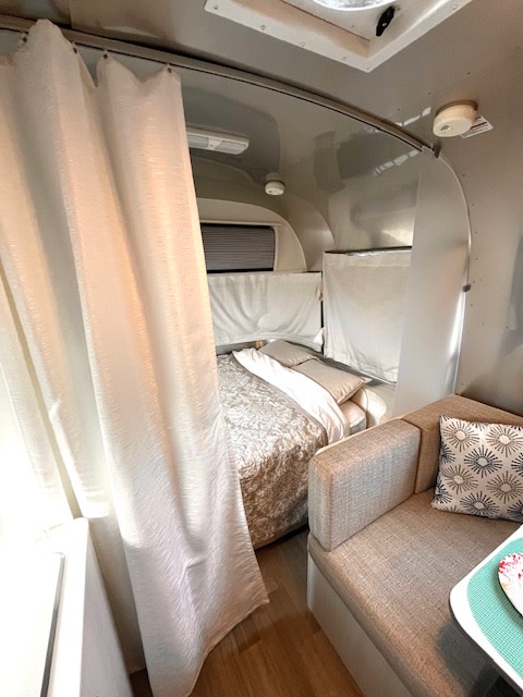 Inside a modern RV rental: bed, privacy curtain, and comfy bench seating. Ideal for compact travel adventures.. Airstream Bambi 2020