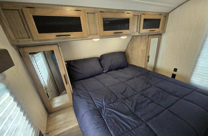 Cozy RV rental bedroom features a comfortable bed with dark blue bedding, overhead storage, and mirrored wardrobes.. Forest River Cherokee Alpha Wolf 2020