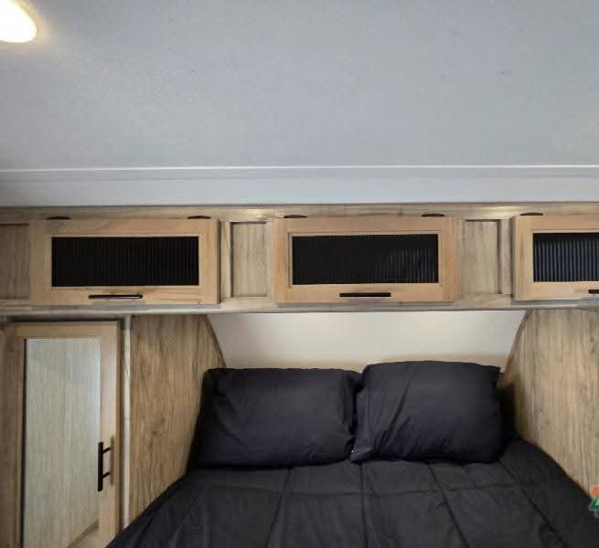Cozy rv rental bedroom with a comfy black bed, overhead wood cabinets, and built-in storage for a relaxing stay.. Forest River Cherokee Alpha Wolf 2020