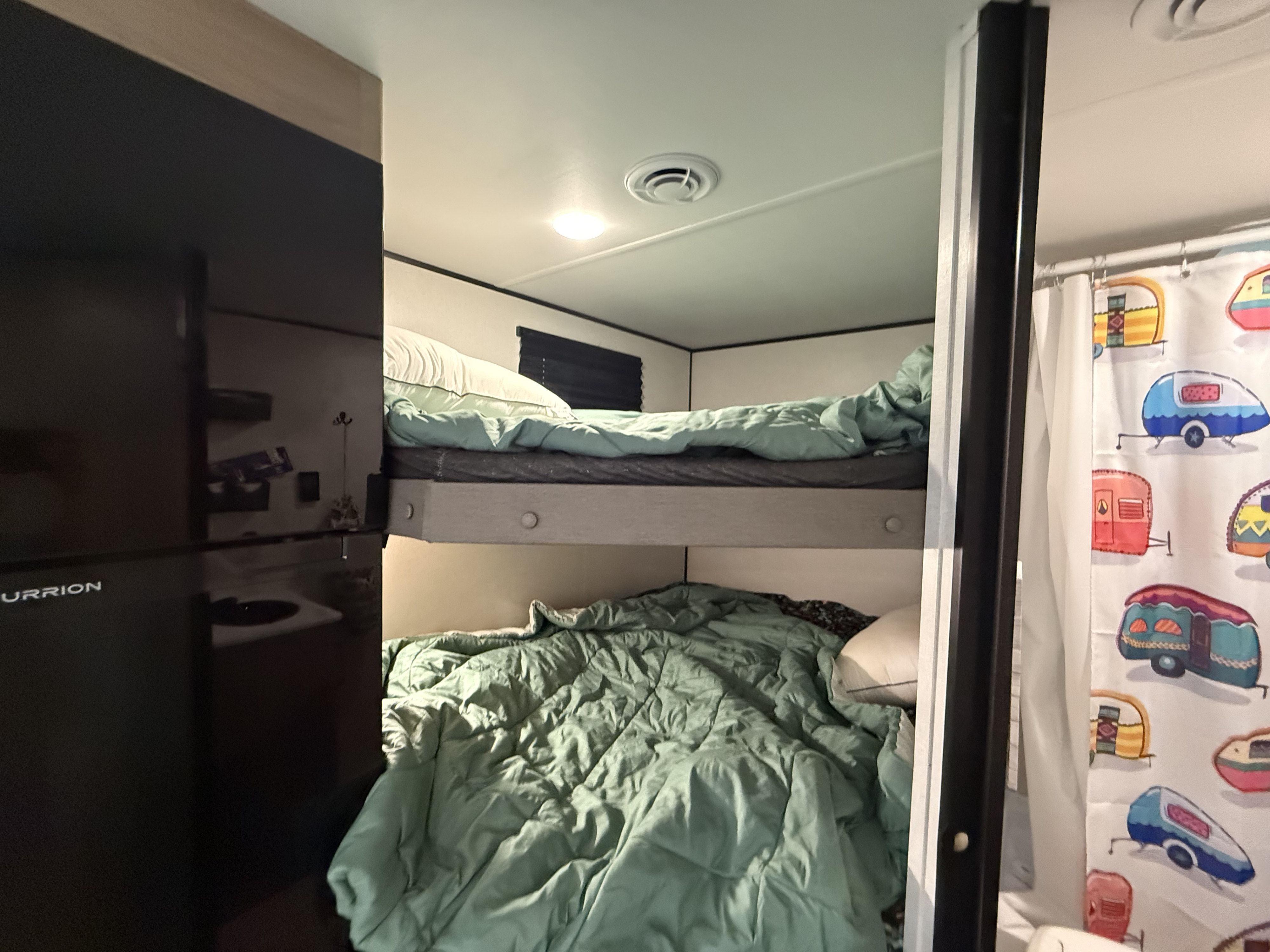 RV rental interior featuring bunk beds with green comforters, a Furrion fridge, and a fun camper-themed shower curtain.. Keystone RV Hideout 2024