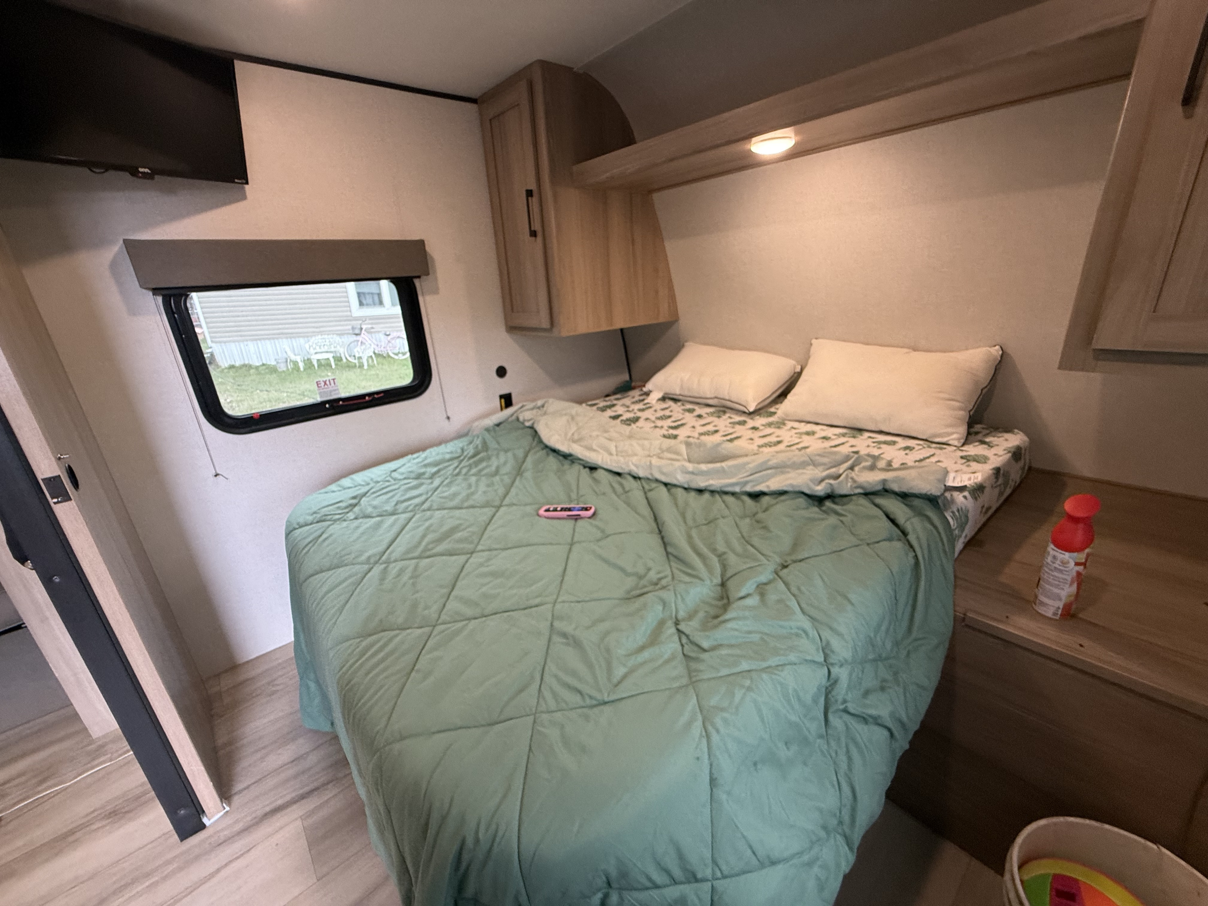 Explore this inviting RV rental bedroom. Features include a cozy bed, TV, overhead storage, and a scenic window view.. Keystone RV Hideout 2024