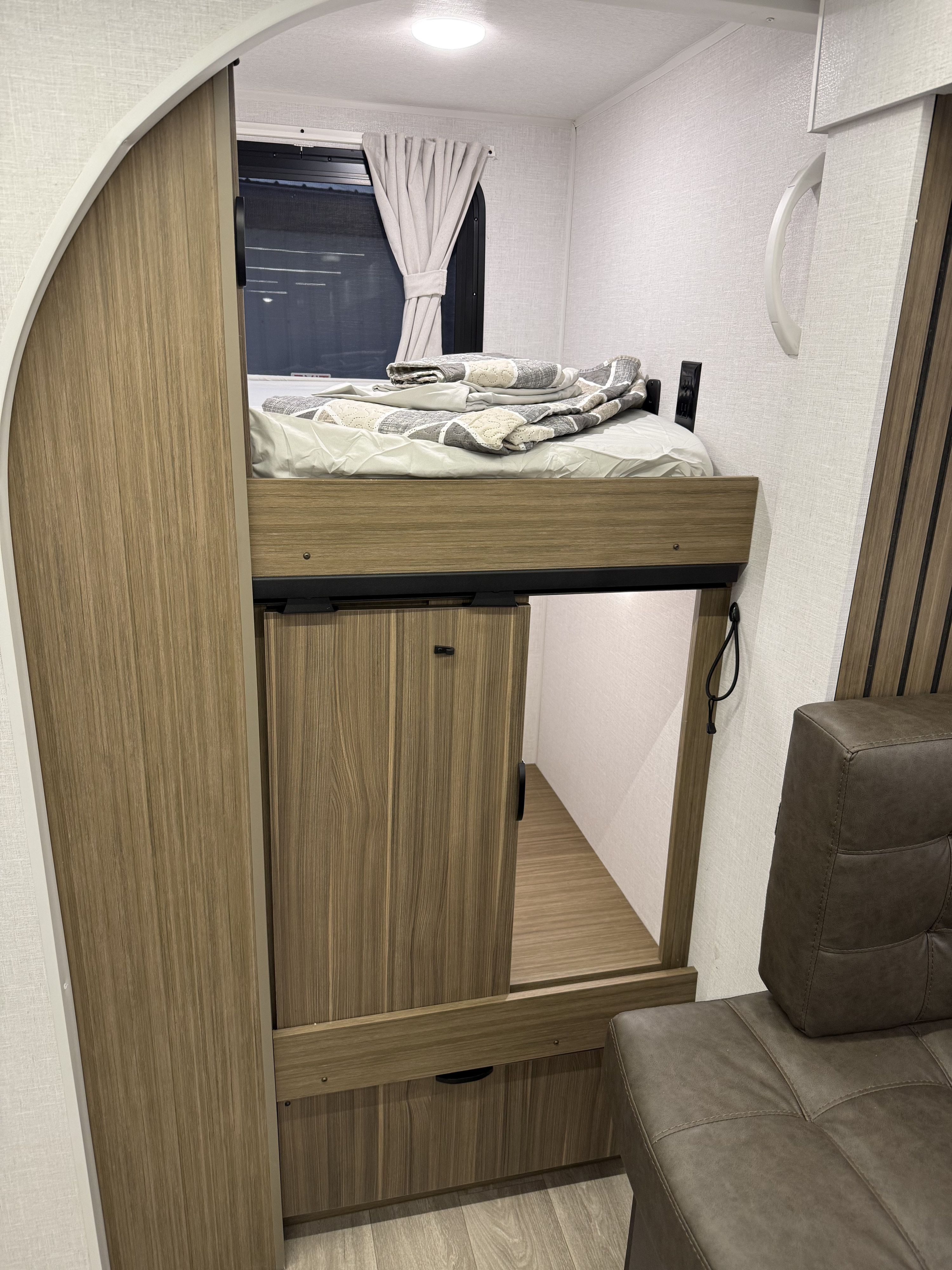 This RV rental interior features a modern bunk bed over storage, with an adjacent brown sofa. Perfect for compact living.. Forest River Salem Cruise-Lite 2026