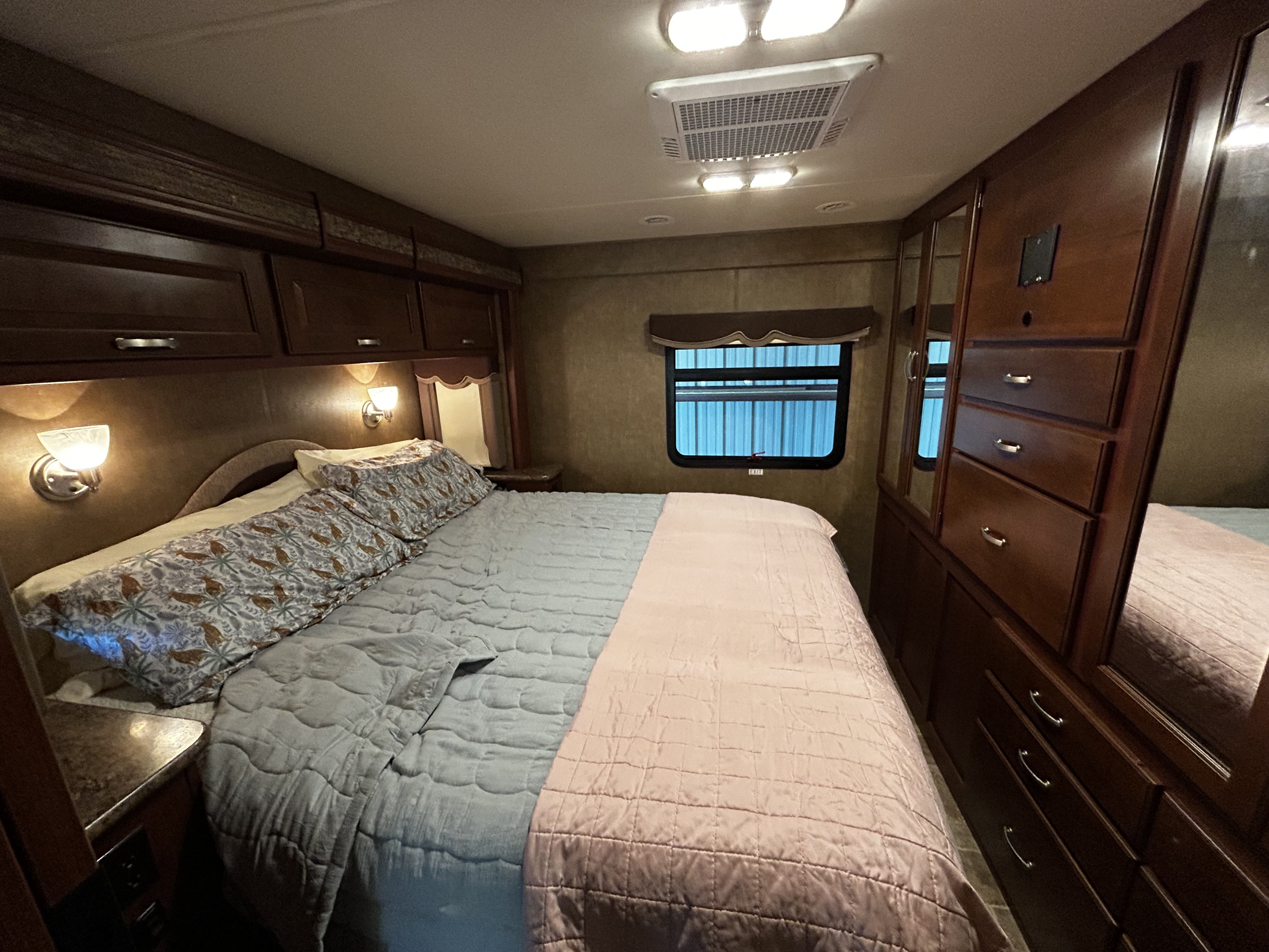 Cozy rv rental bedroom featuring a large bed, dark wood storage, and bright overhead lights. Perfect for comfortable journeys.. Thor Four Winds 2015