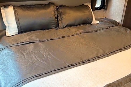 Enjoy a comfortable night's rest in this RV rental's cozy bedroom, featuring a gray comforter and pillows.. Thor Hurricane 2022