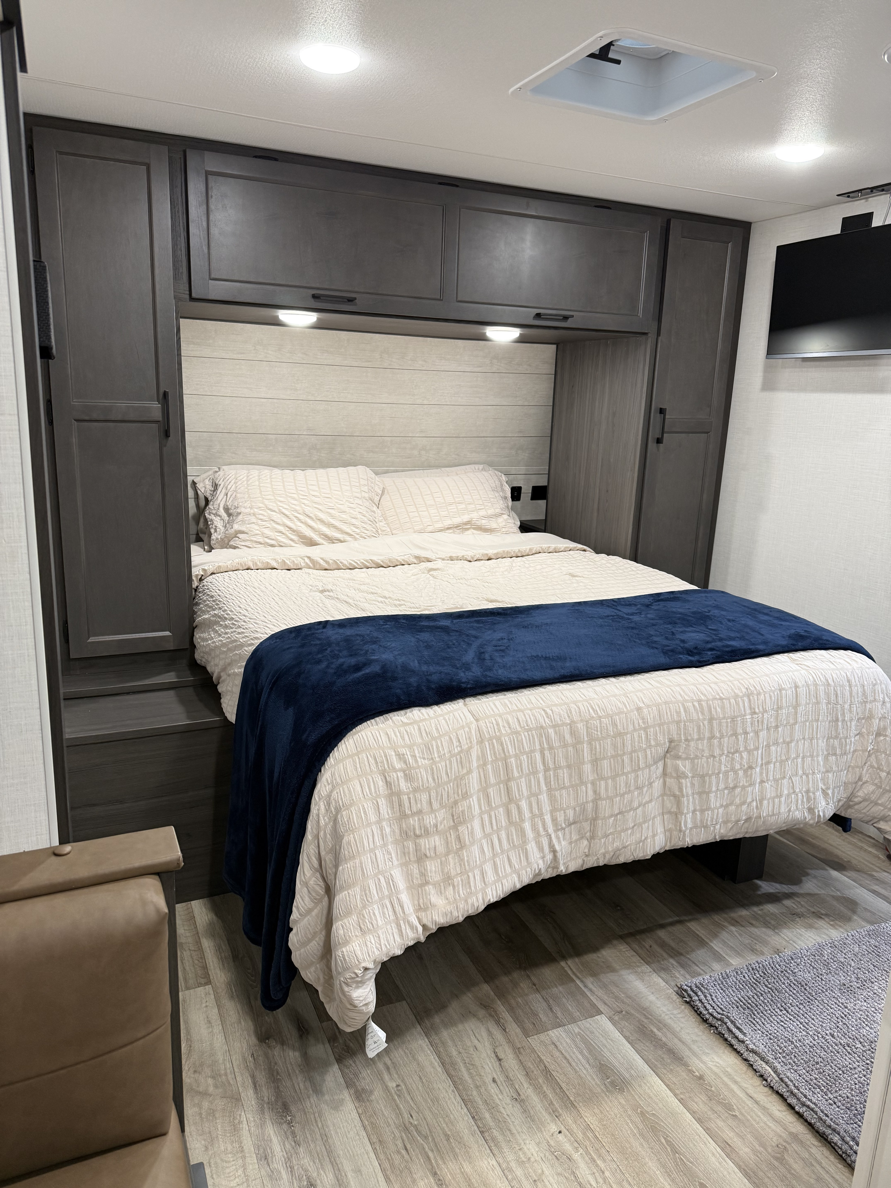 Clean, modern RV rental bedroom featuring a queen bed, built-in storage, TV, and overhead lighting.. KZ Stratus 2025