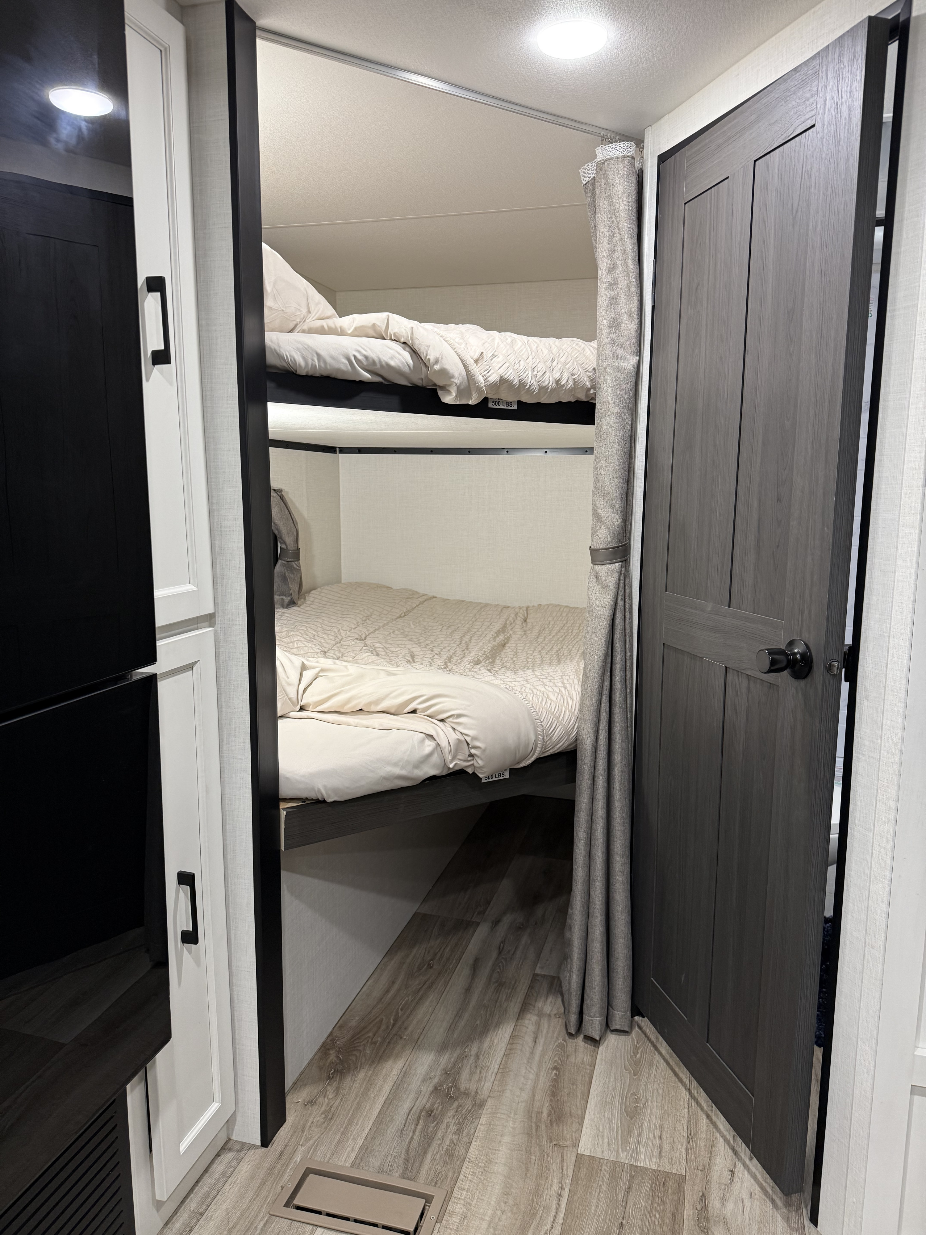 RV rental bunk beds: two compact berths with light bedding, a privacy curtain, and a visible 500 lbs weight limit.. KZ Stratus 2025