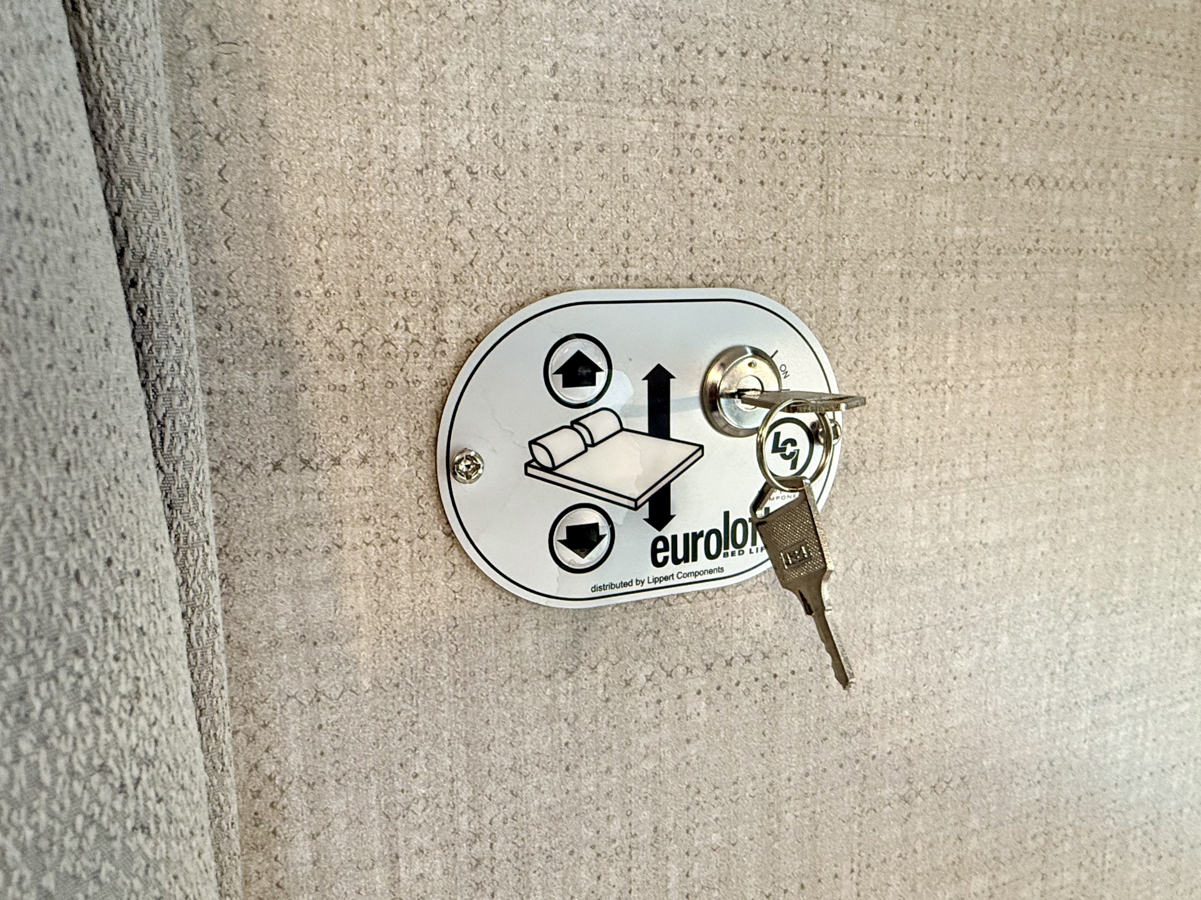 RV rental bed lift control panel with key inserted, featuring up/down arrows & bed icon for height adjustment.. Thor Tiburon 2023
