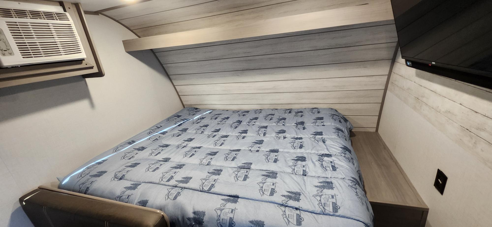 Cozy RV rental bedroom with camping-themed comforter, AC, and TV. Ideal for travel trailer stays.. Dutchmen Coleman Lantern LT 2023