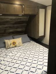 Cozy RV rental bedroom interior features a comfortable bed with patterned bedding, overhead storage, and mirror.. Keystone RV Passport GT 2021