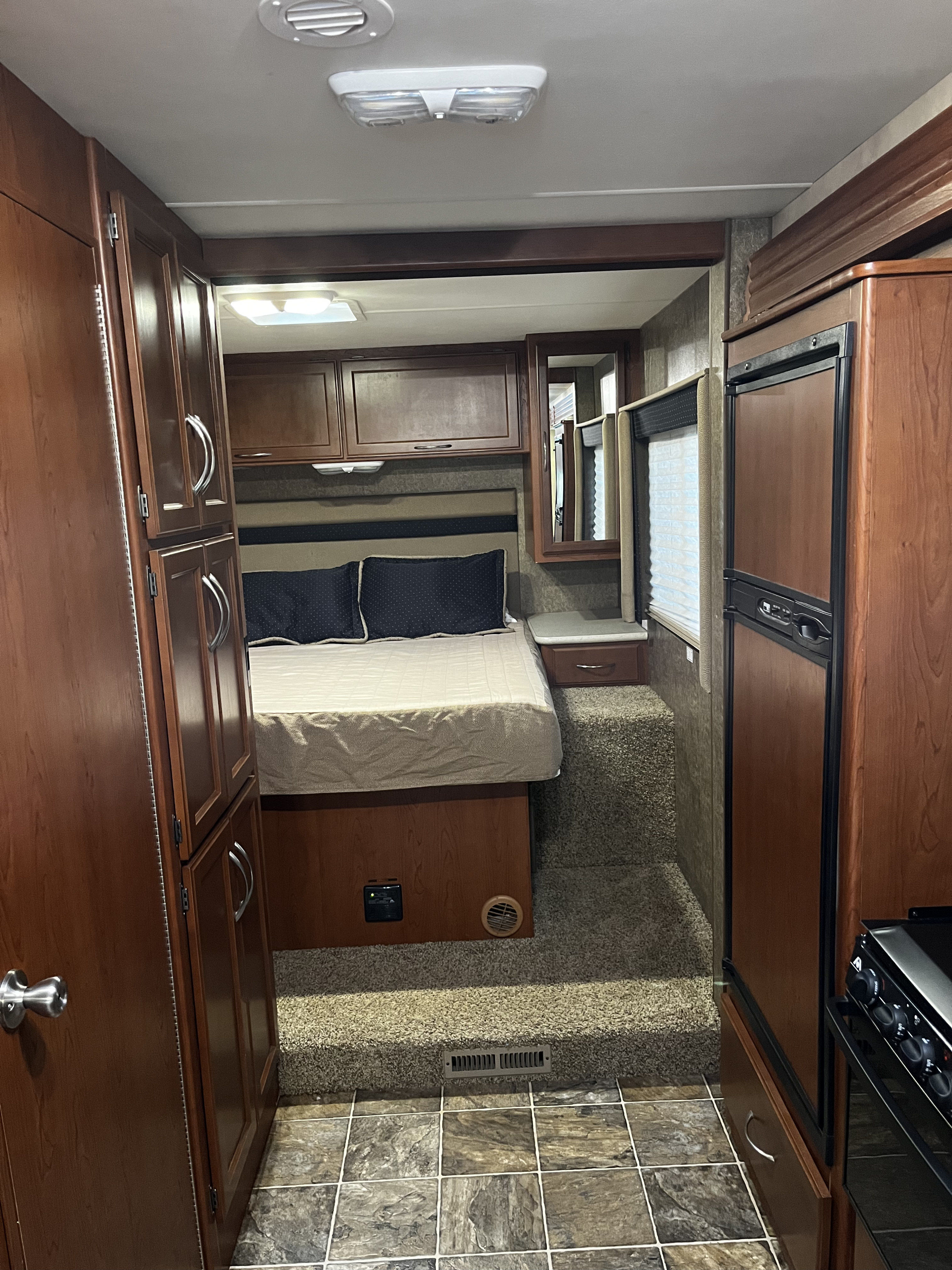 Inside this rv rental, a raised bedroom platform with wood cabinets, tiled and carpeted floors, and a small kitchen with fridge.. A.C.E. A.C.E. Motorhome 2013