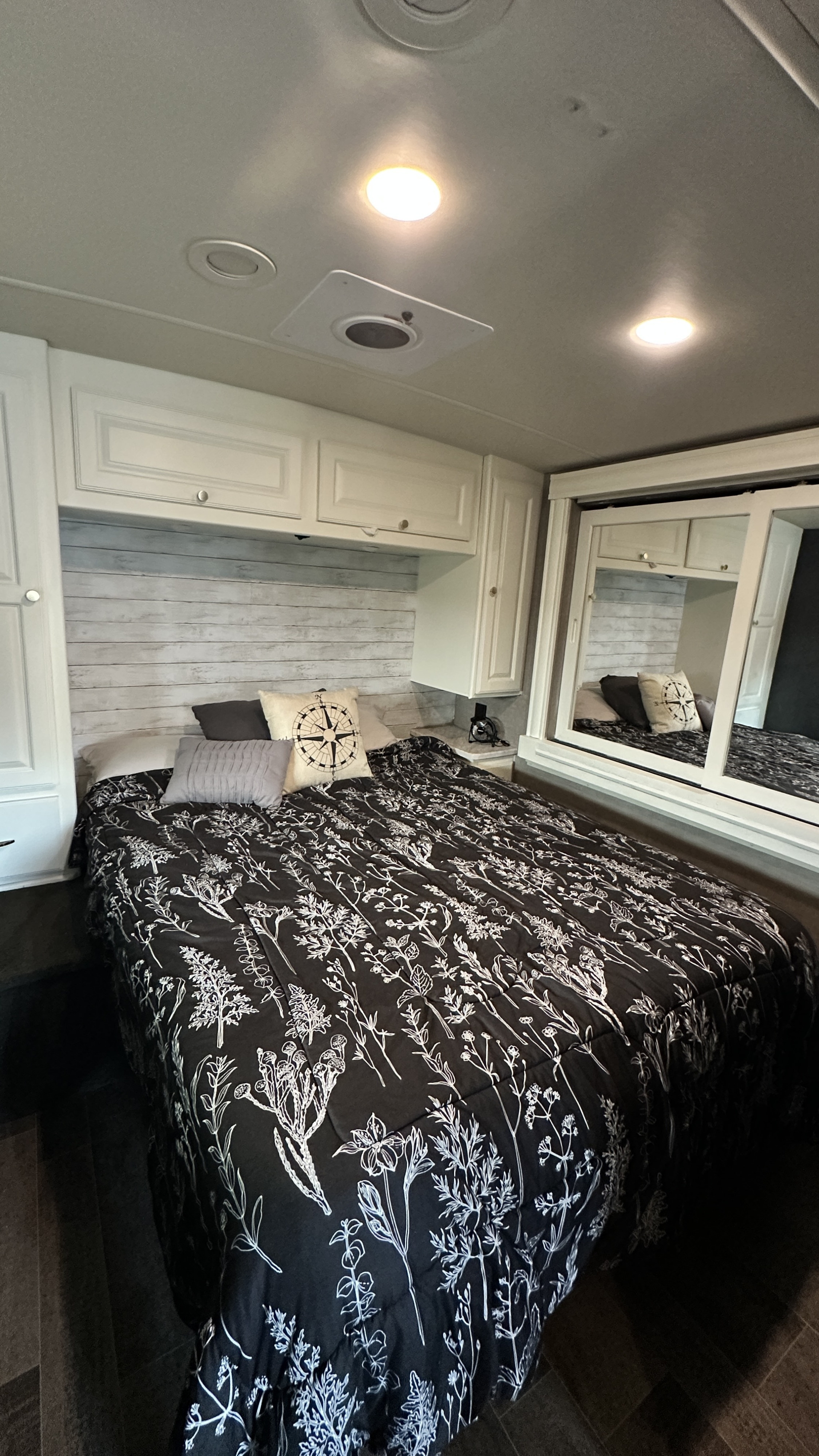 Relaxing RV rental bedroom showcasing a bed with botanical print comforter, wood plank accent wall, and storage.. Winnebago Vista LX 2019