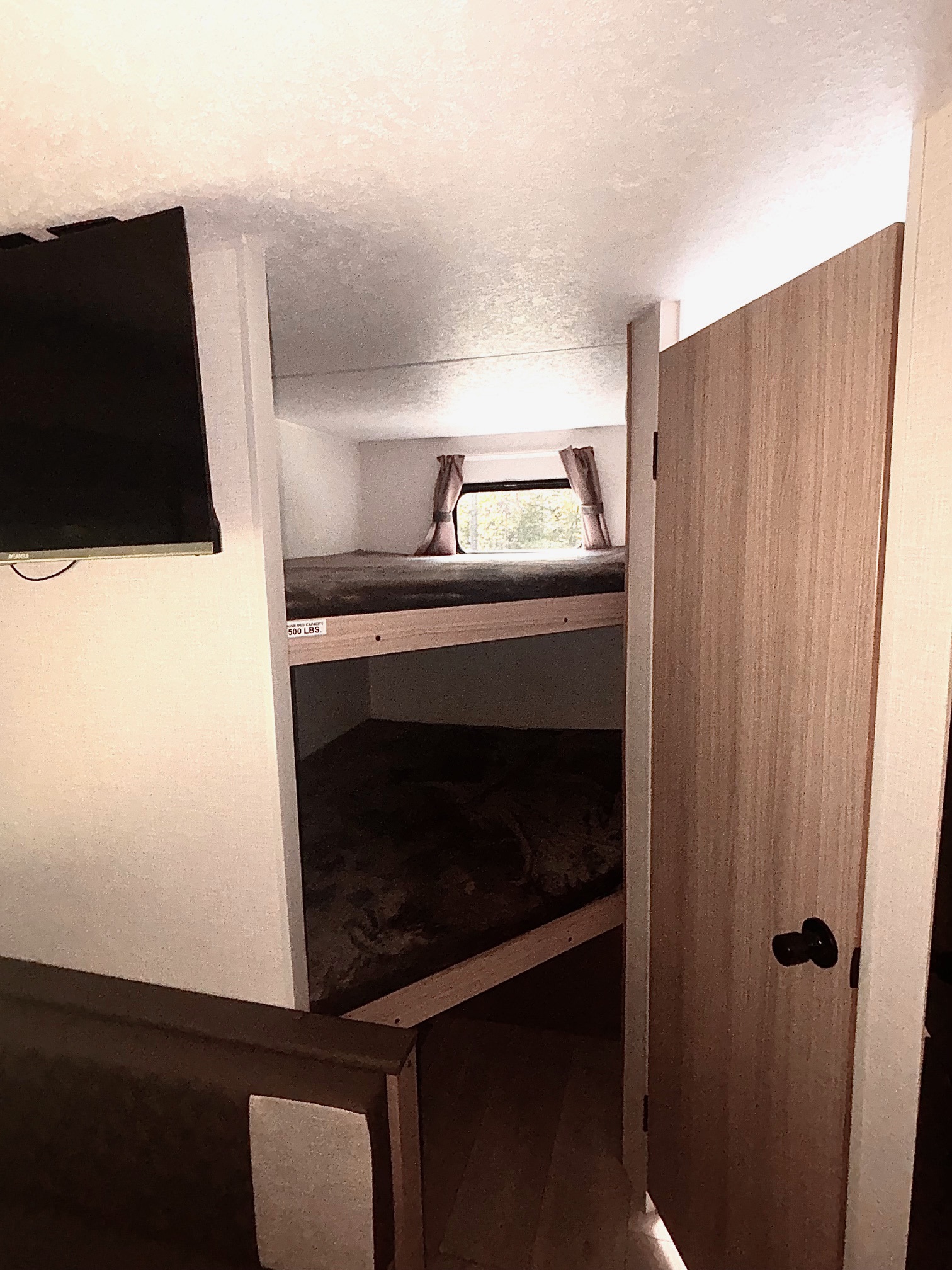 Cozy RV rental interior with bunk beds, a TV, and a partial door. Ideal for compact travel and sleeping.. KZ Sportsmen Select 2025