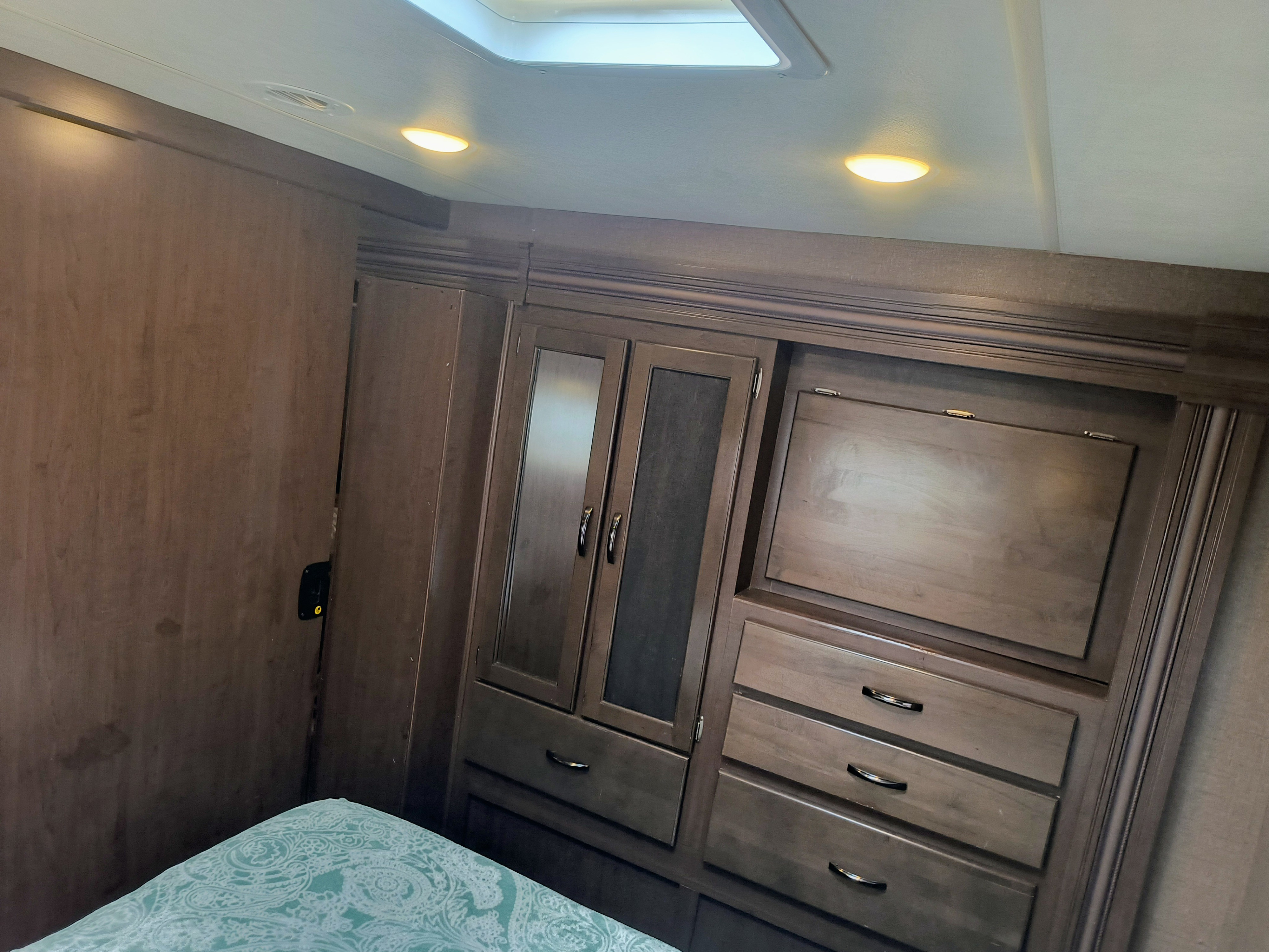 Visually impaired users: this RV rental bedroom features dark wooden built-in cabinets, drawers, and overhead lighting above a bed.. Thor Motor Coach Freedom Elite 2019