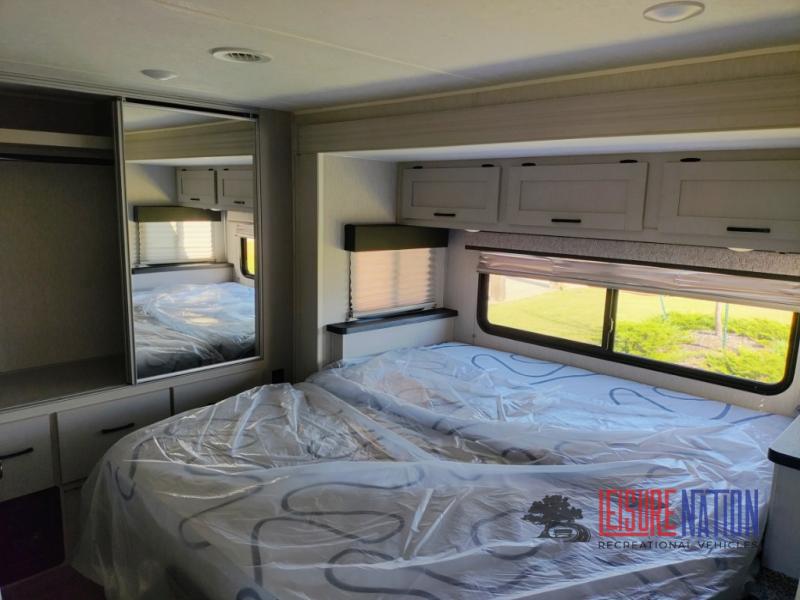 Clean RV rental bedroom featuring a large bed, mirrored closet, and overhead cabinets for a comfortable stay.. Coachmen Freelander 2023
