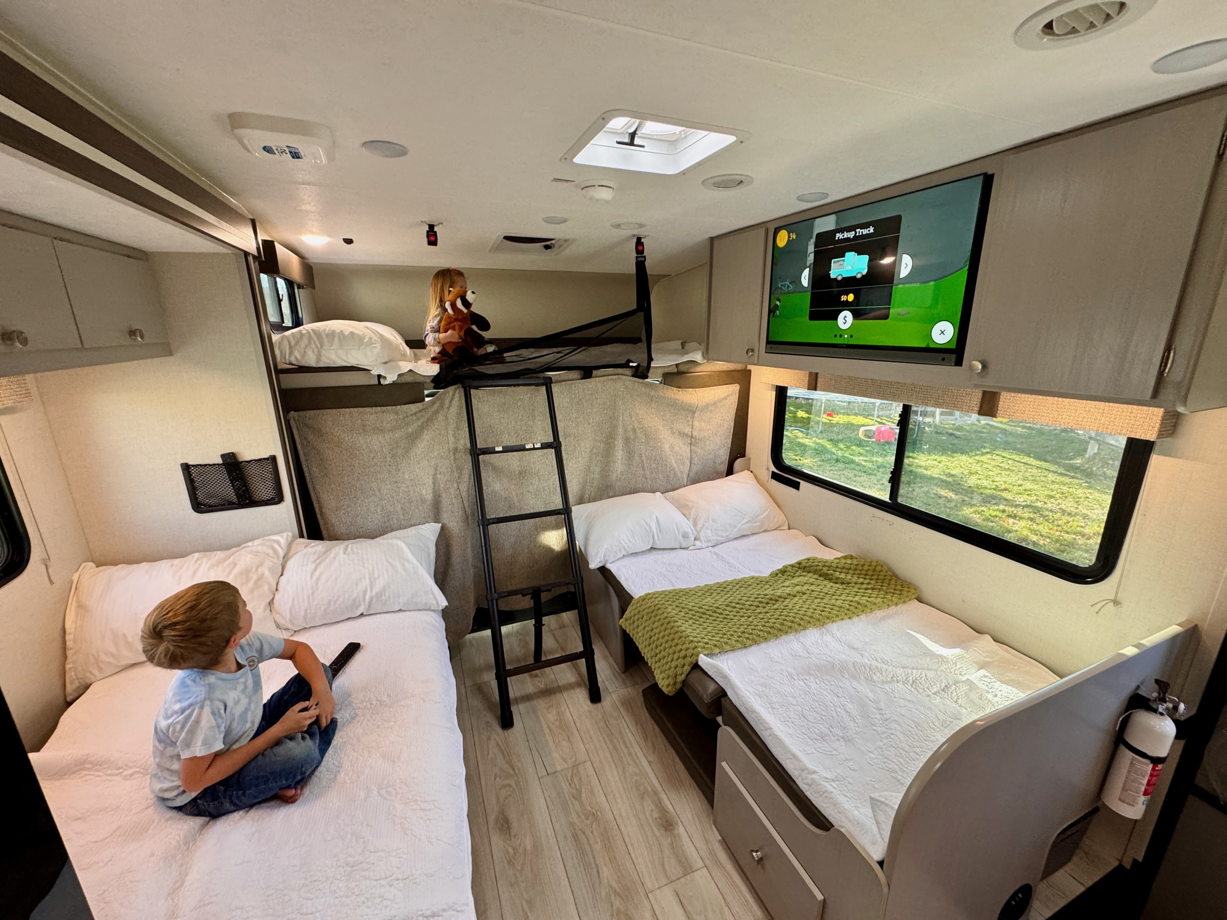 Kids inside a family RV rental. A boy watches TV on a lower bed, and a girl plays in the upper bunk. Spacious interior for camping adventures.. Forest River Coachmen Freelander 2025