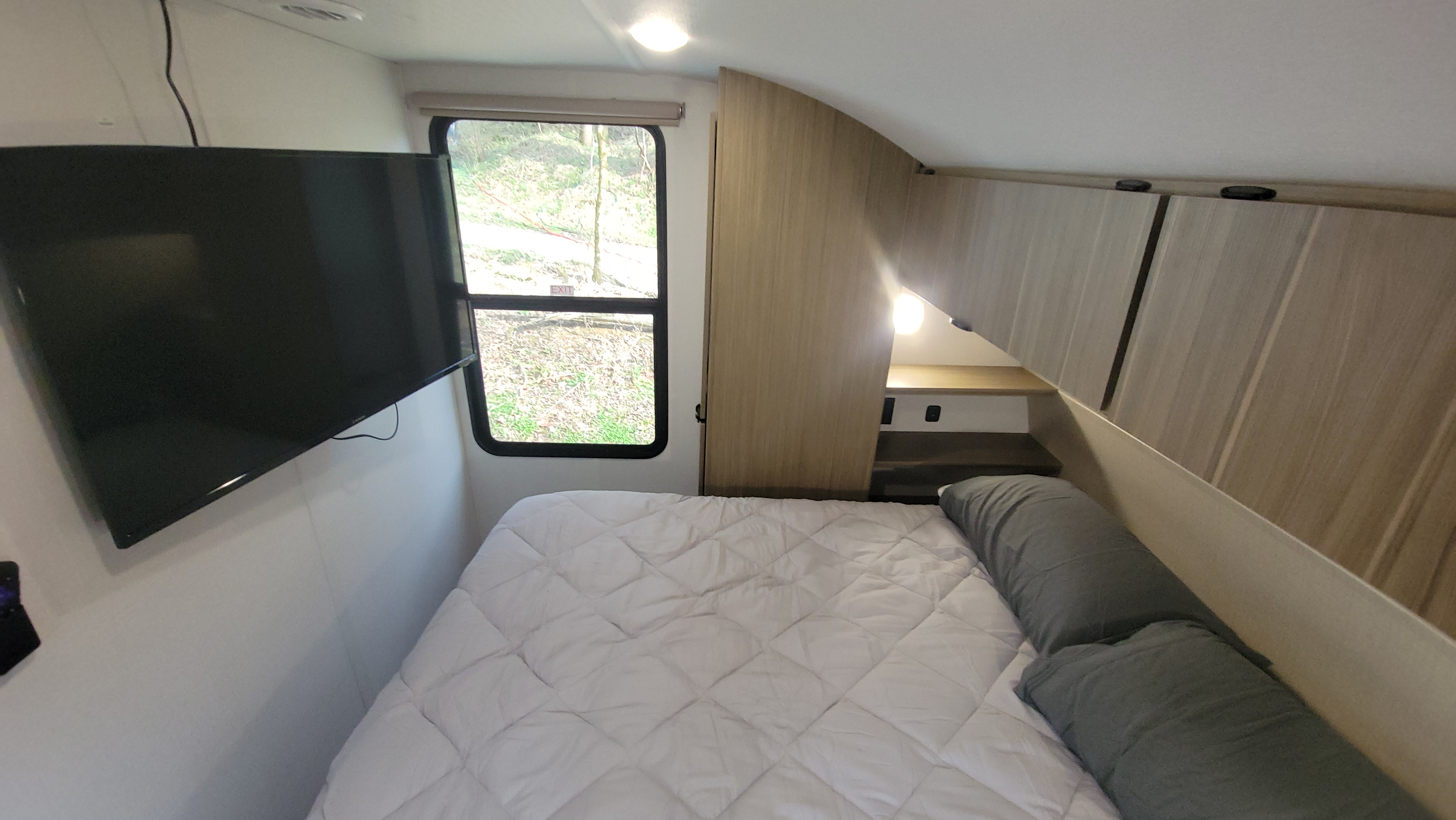 An RV rental bedroom with a comfy bed, wall-mounted TV, window overlooking nature, and overhead cabinets for storage.. Forest River Salem Cruise-Lite 2025