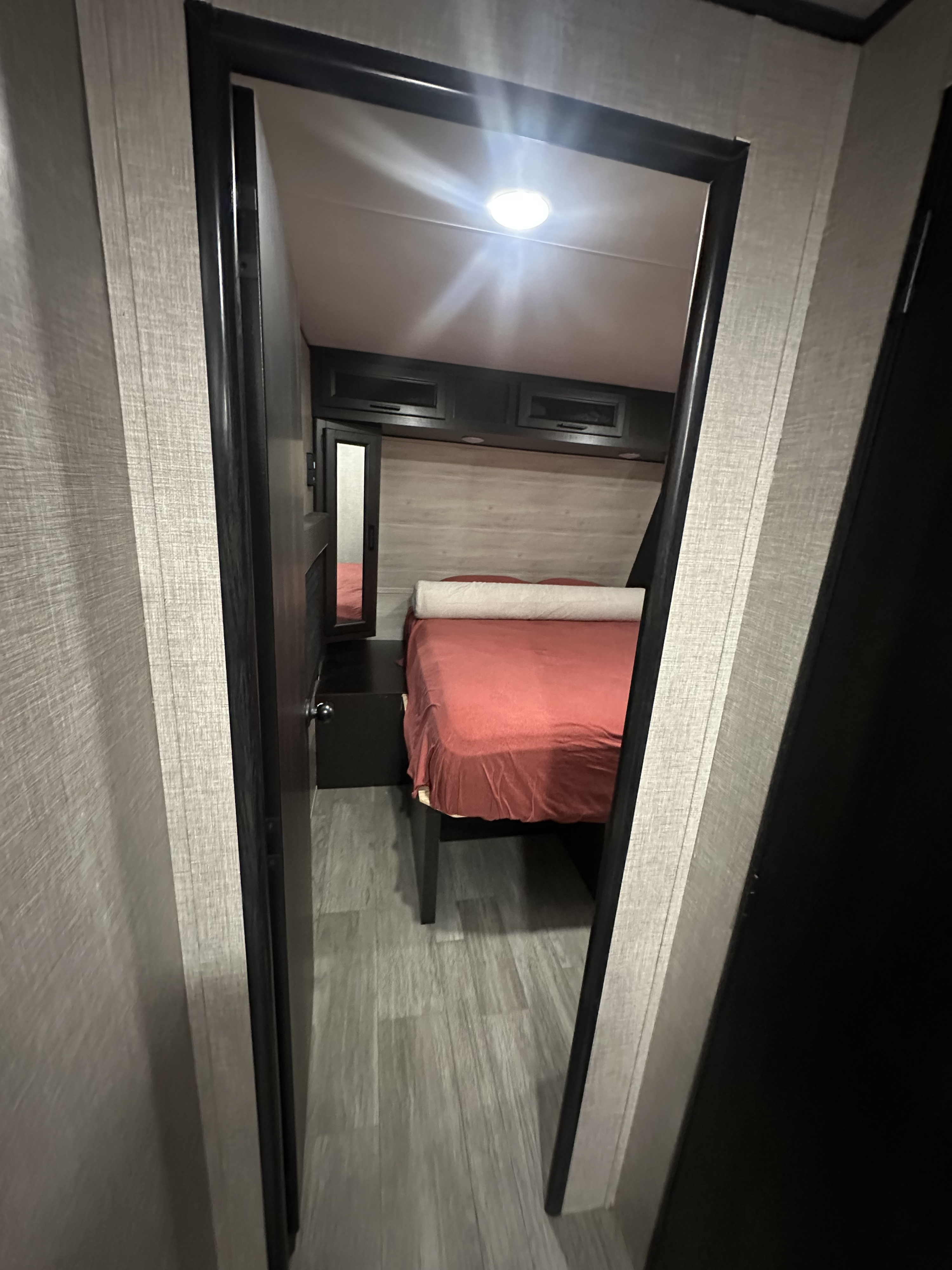 Peek inside this cozy RV rental's compact bedroom, featuring a bed with red linens, overhead cabinets & light wood-look flooring.. Jayco Jay Flight 2022