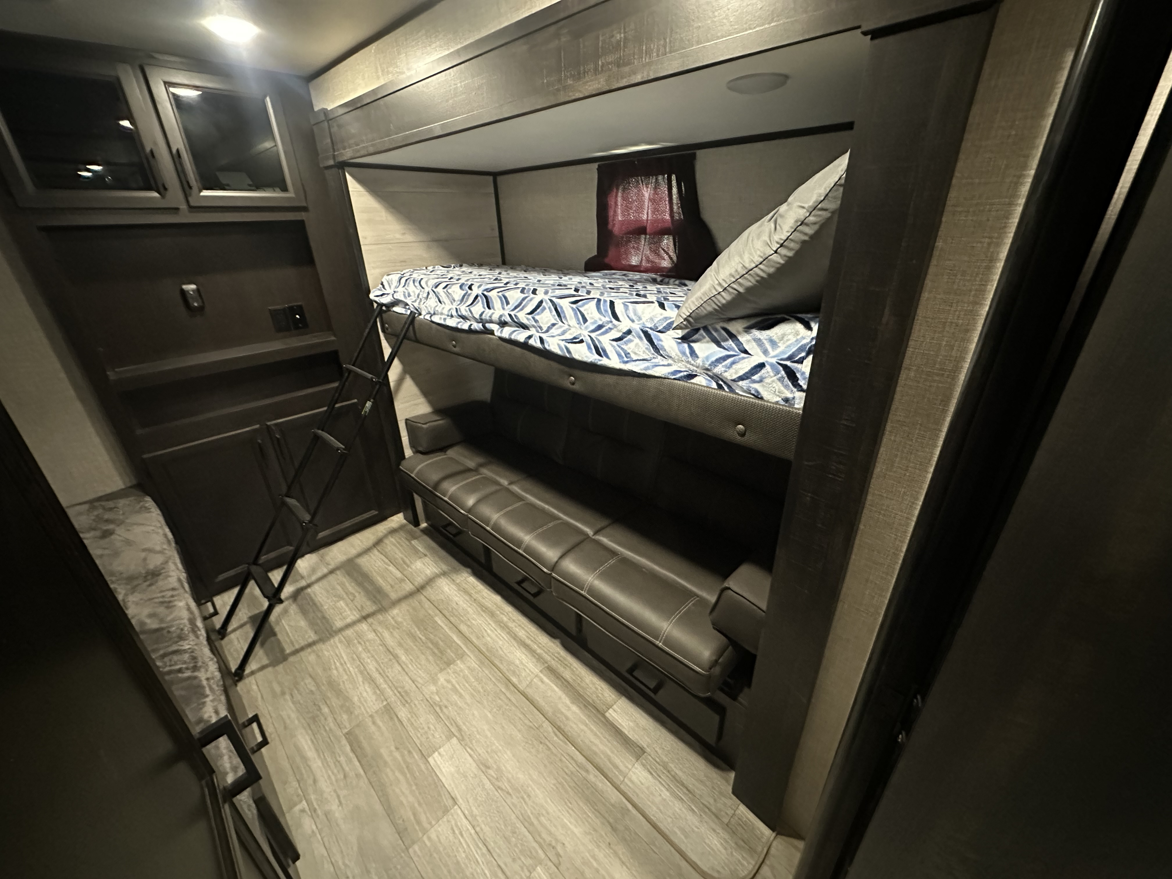 Cozy RV rental bunk bed area: top bunk, convertible sofa below, ladder, cabinets, and wood-look flooring.. Jayco Jay Flight 2022