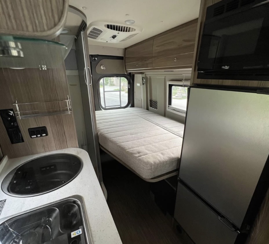 Explore this RV rental's inviting interior: compact kitchen, cozy bed, fridge, and microwave for comfortable travels.. Winnebago Travato 2020