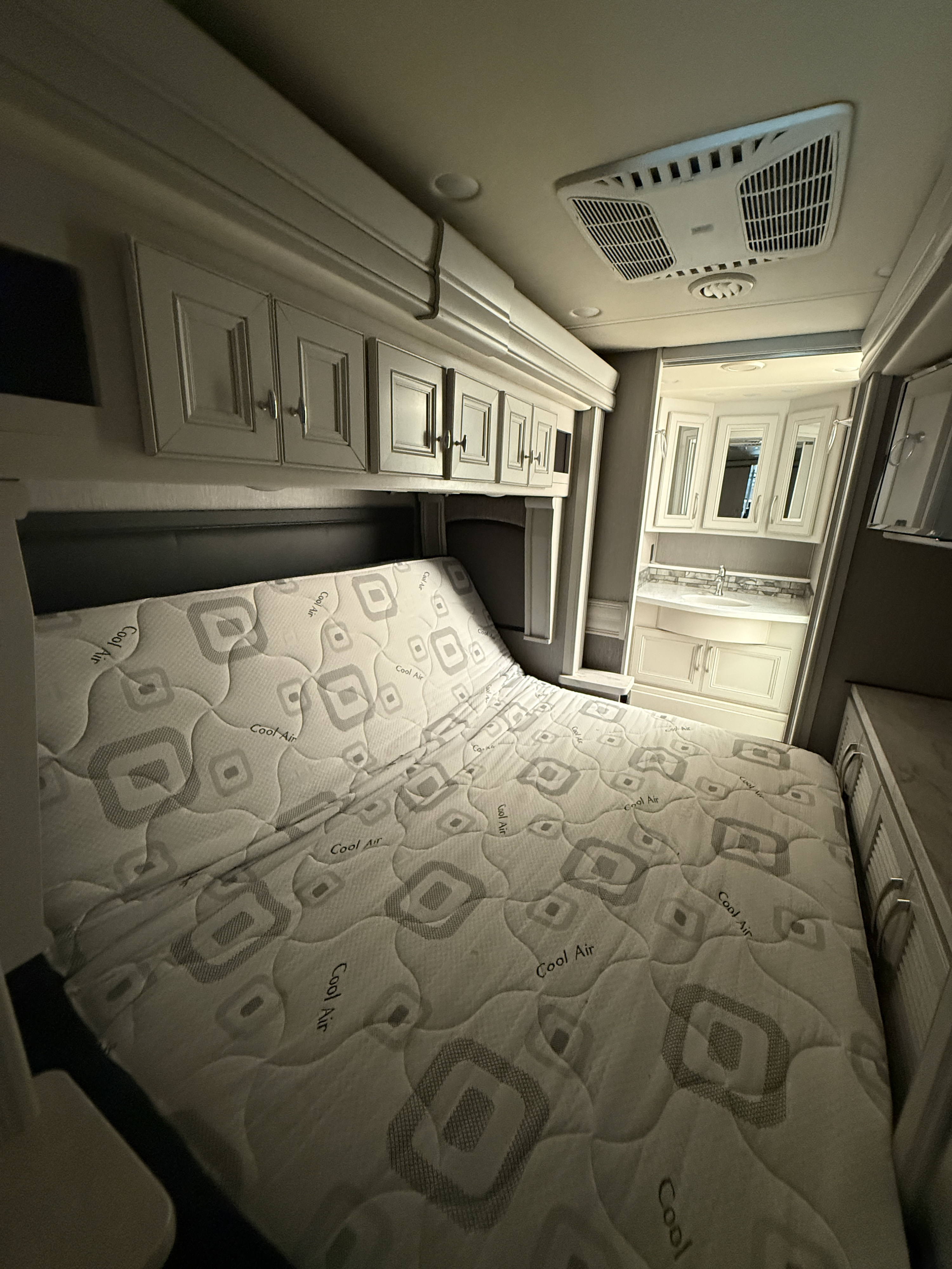 "Cool Air" mattress in an **rv rental** bedroom, with overhead storage & a compact vanity visible in the modern RV interior.. Holiday Rambler Navigator 2022