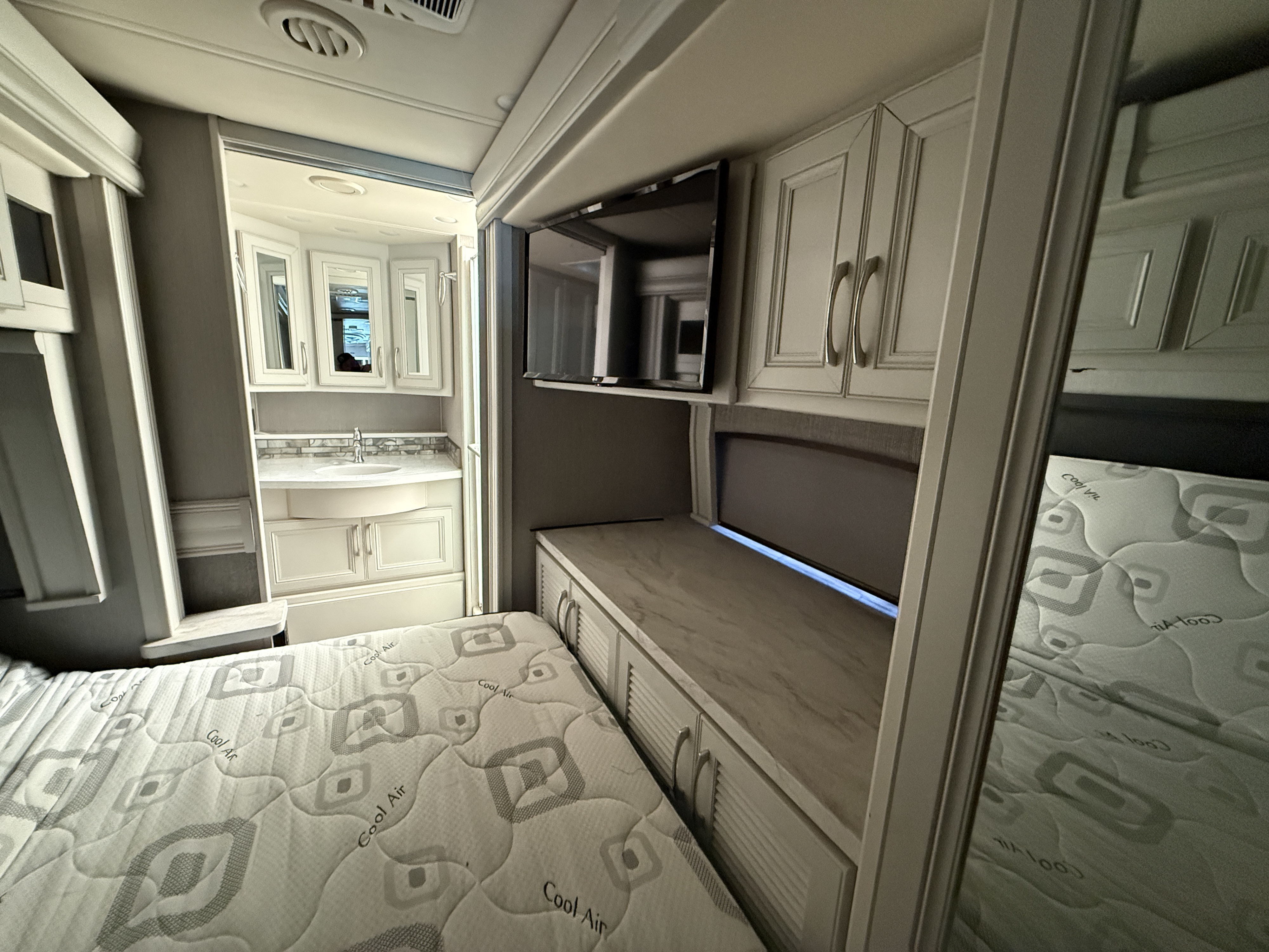 Modern RV rental interior with a cozy bedroom, "Cool Air" mattress, TV, ample storage, and an accessible bathroom vanity.. Holiday Rambler Navigator 2022
