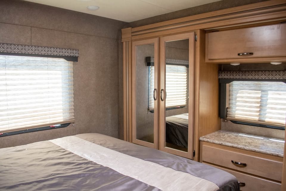 Cozy RV rental bedroom featuring a comfortable bed, mirrored wardrobe, and windows with blinds for natural light.. Thor Four Winds 31EV 2020