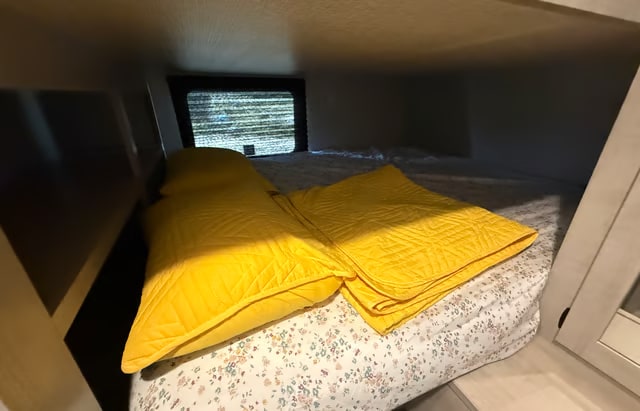 Cozy RV rental bunk bed with bright yellow quilted pillows, a matching blanket, and floral sheets, perfect for rest.. Crossroads RV Zinger 2025