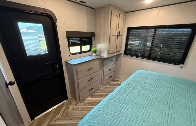 Inside this spacious RV rental bedroom, find a comfy teal bed, ample storage, and windows for scenic views.. Crossroads RV Zinger 2025