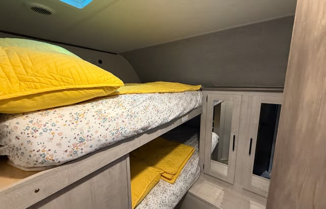 Bright yellow pillows and blankets on floral bunk beds inside a cozy RV rental. Ideal for family adventures.. Crossroads RV Zinger 2025