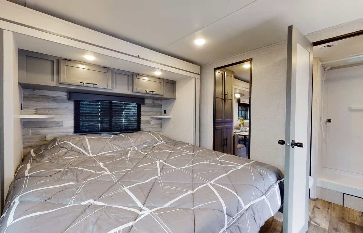 Modern RV rental bedroom: cozy bed with geometric comforter, overhead cabinets, and wood accent wall. Compact travel comfort.. Crossroads RV Volante 2023