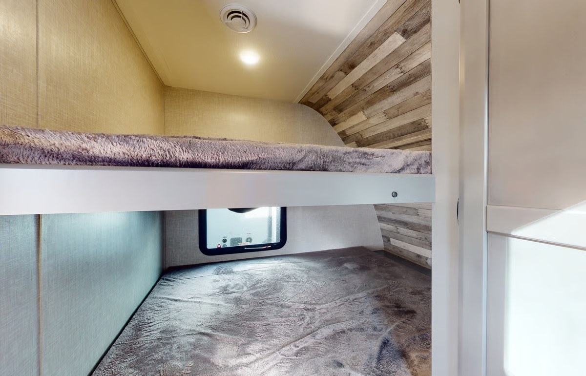 Inside an rv rental, two stacked bunk beds feature soft gray bedding, a small window, and wood-look accent walls. Compact & practical.. Crossroads RV Volante 2023