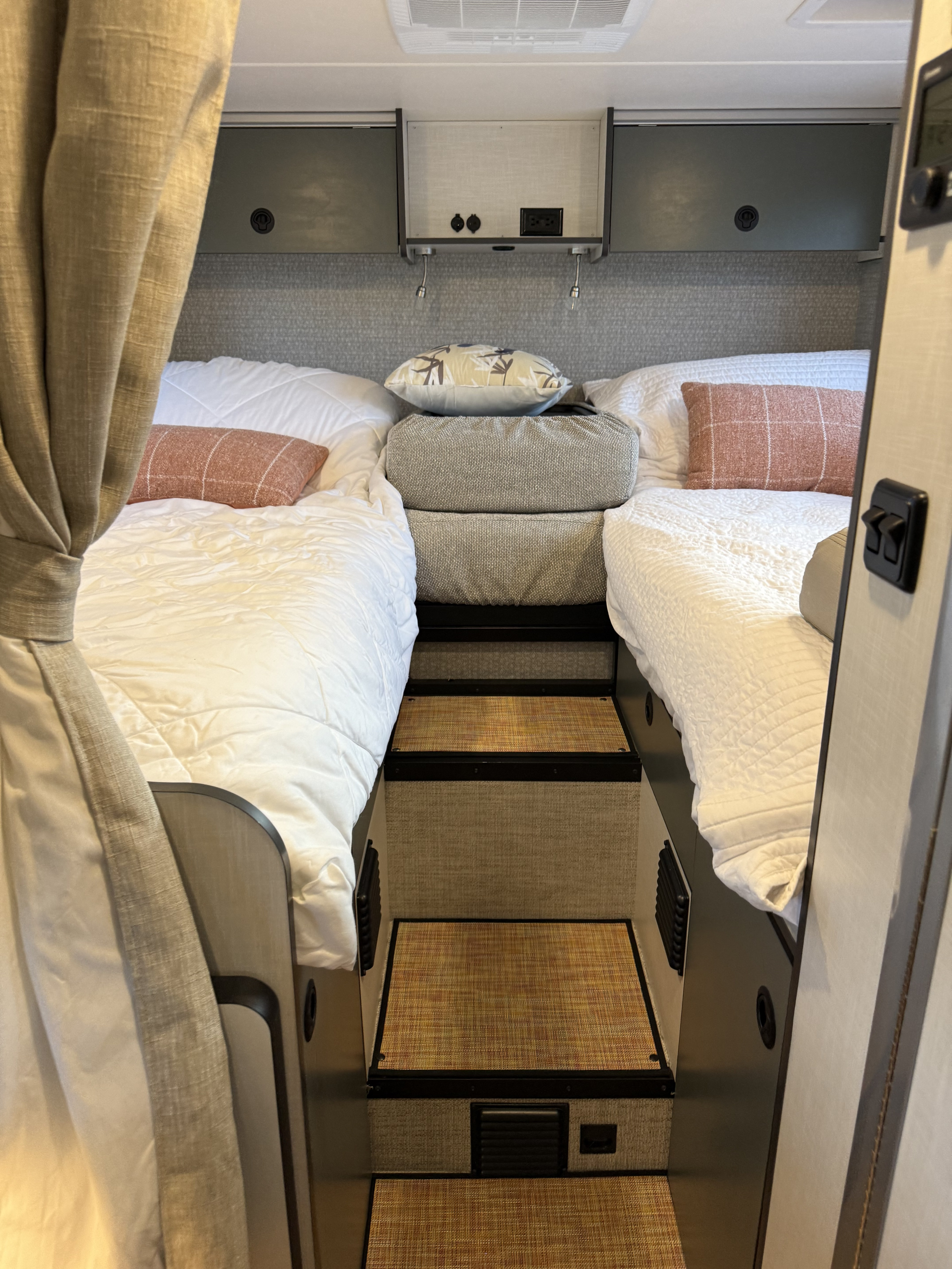 A well-appointed RV rental bedroom with two comfortable twin beds, steps, and convenient overhead storage.. Winnebago Ekko 2025