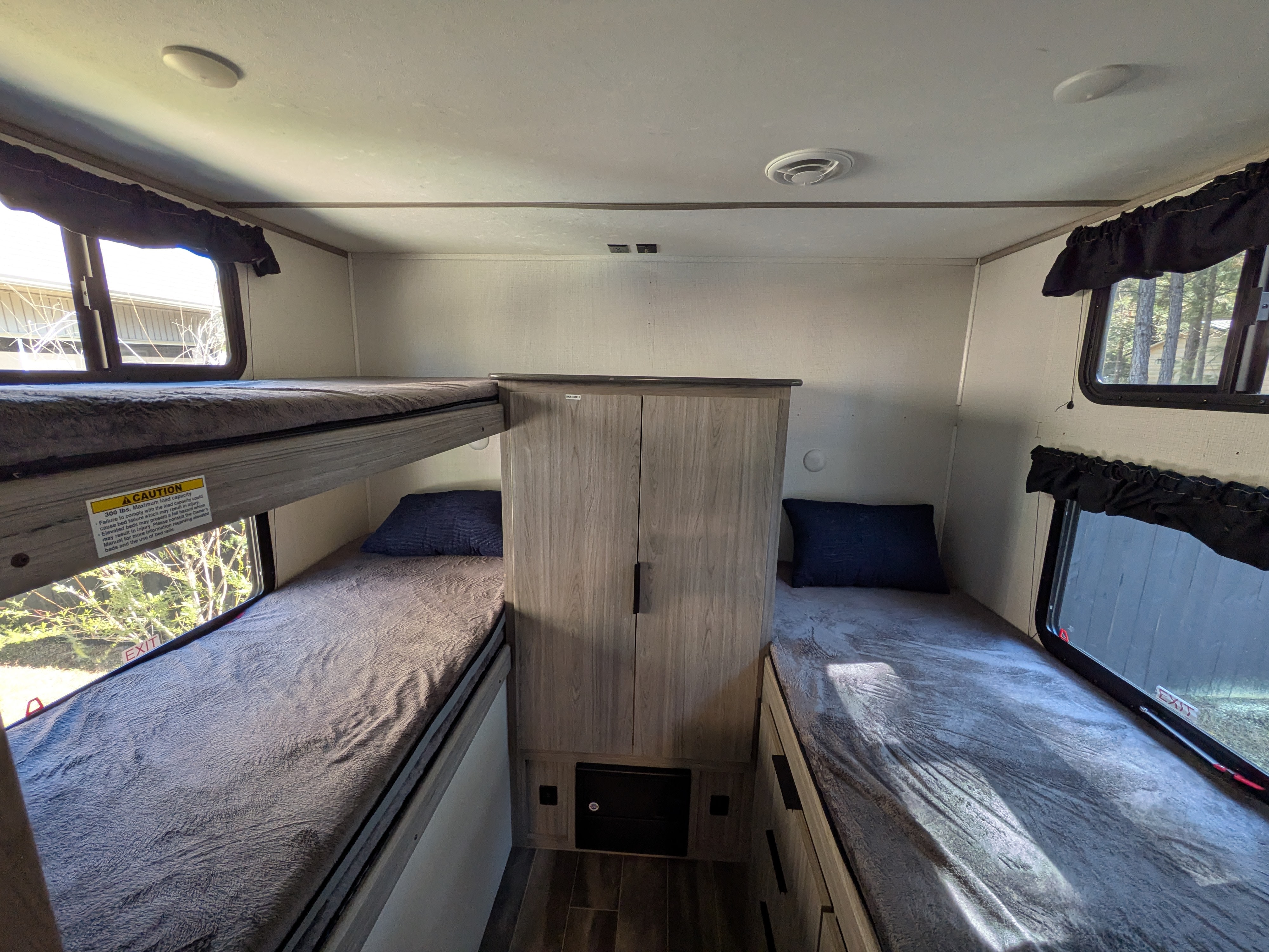 Cozy bunk beds and a single bed in an RV rental sleeping area, with window views and a cabinet.. Keystone RV Passport SL 2021