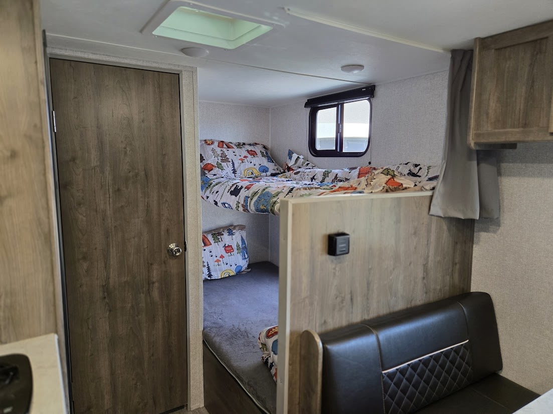 Inside this RV rental, find colorful bunk beds with fun patterns, a door, and a comfy dinette bench. Ideal for families.. Aspen Trail LE 2020