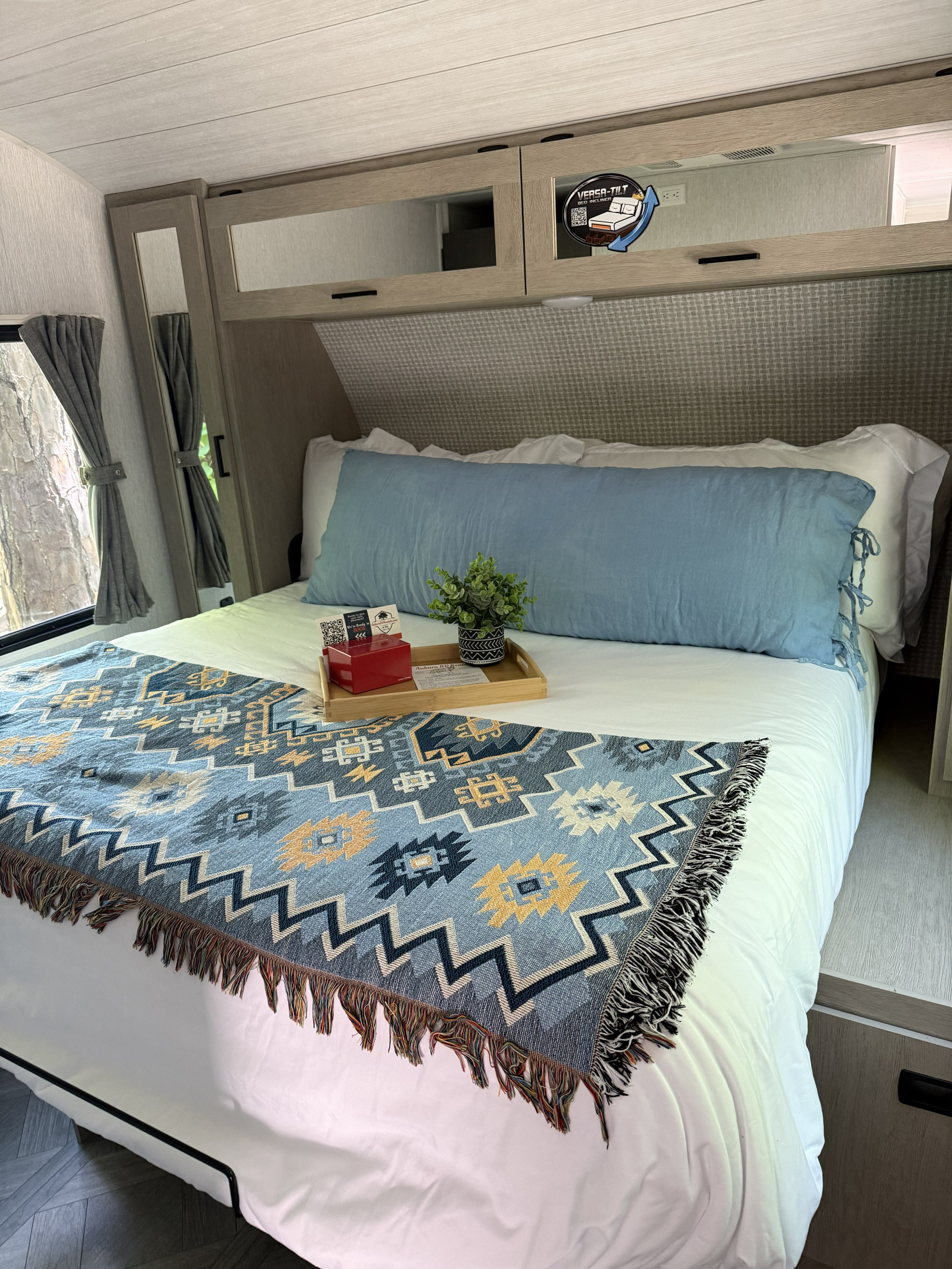Cozy RV rental bedroom features a comfy bed with a blue pillow, patterned throw, and Versa-Tilt bed incliner. Overhead storage.. Forest River Salem 2024