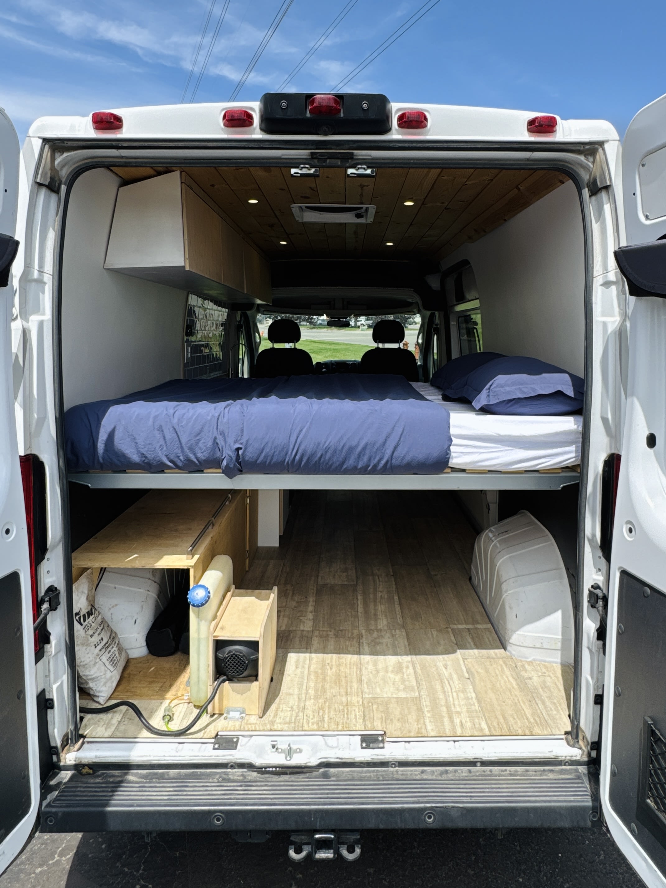 Inside an RV rental, a cozy campervan conversion features an elevated bed and organized storage for van life adventures.. Dodge ProMaster 2019