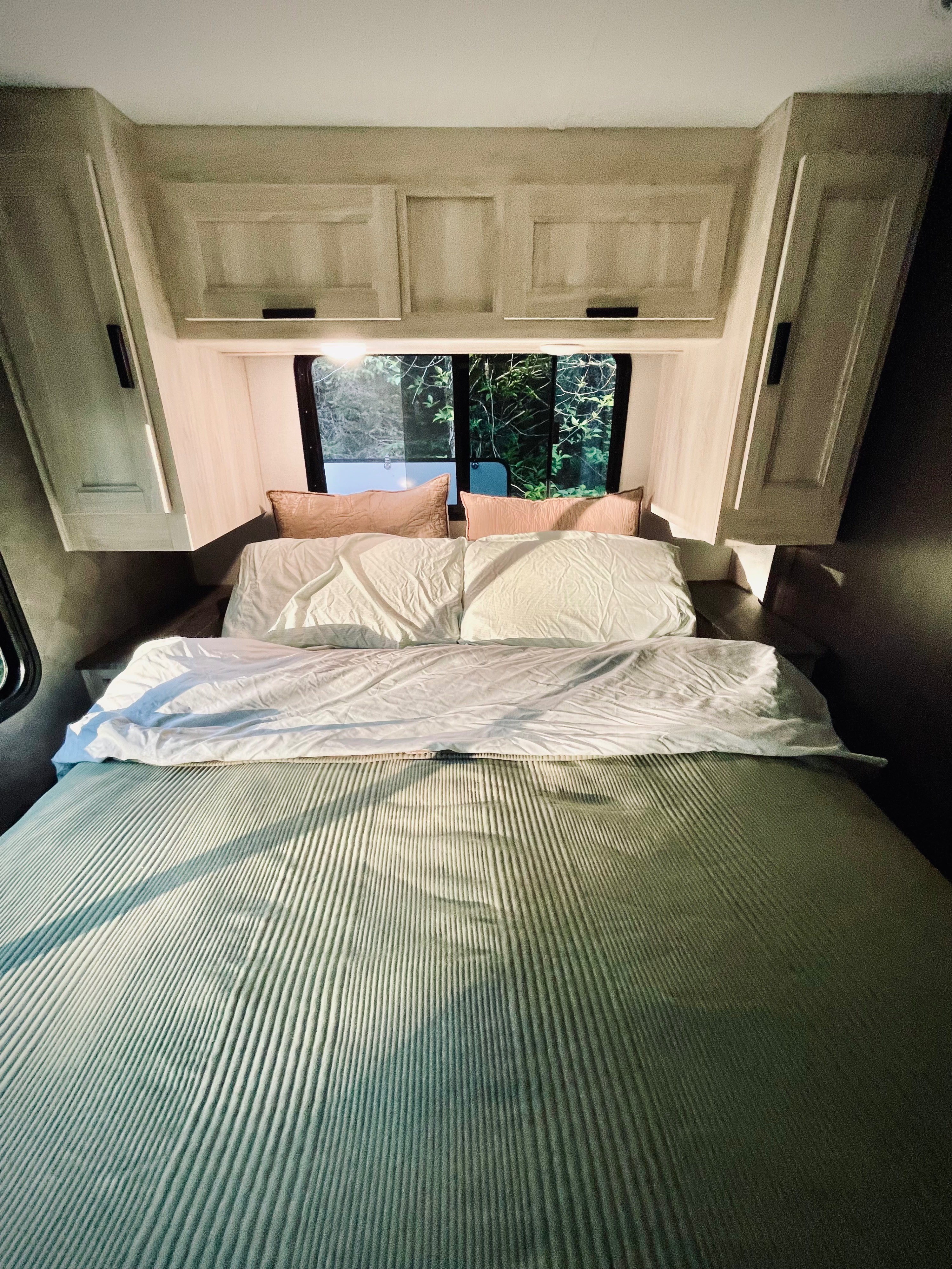 Cozy RV rental bedroom featuring a bed with ribbed bedding, white pillows, and a bright window view of nature.. Forester LE 2022