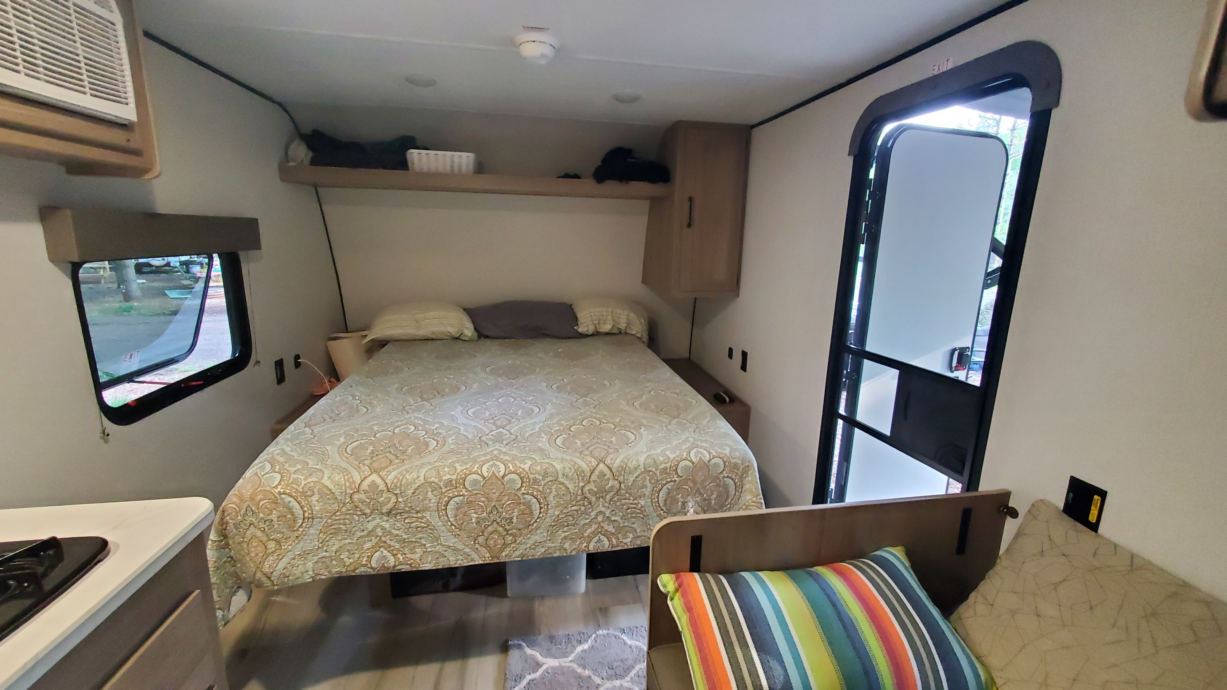 Inside this rv rental, a compact and cozy bedroom features a patterned bedspread, window, and adjacent living space.. Keystone RV Coleman 2025