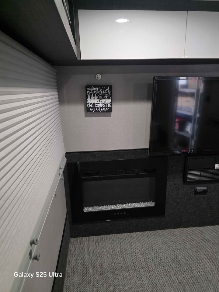 Inside this RV rental: an electric fireplace, TV, and "making memories" decor next to a pleated blind, offering a cozy space.. InTech RV Luna 2022
