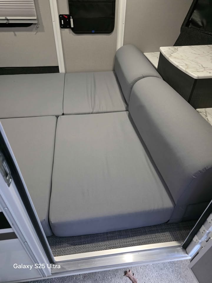 Inside an RV rental, featuring grey cushion seating and a convertible bed, adjacent to a small counter and entry.. InTech RV Luna 2022