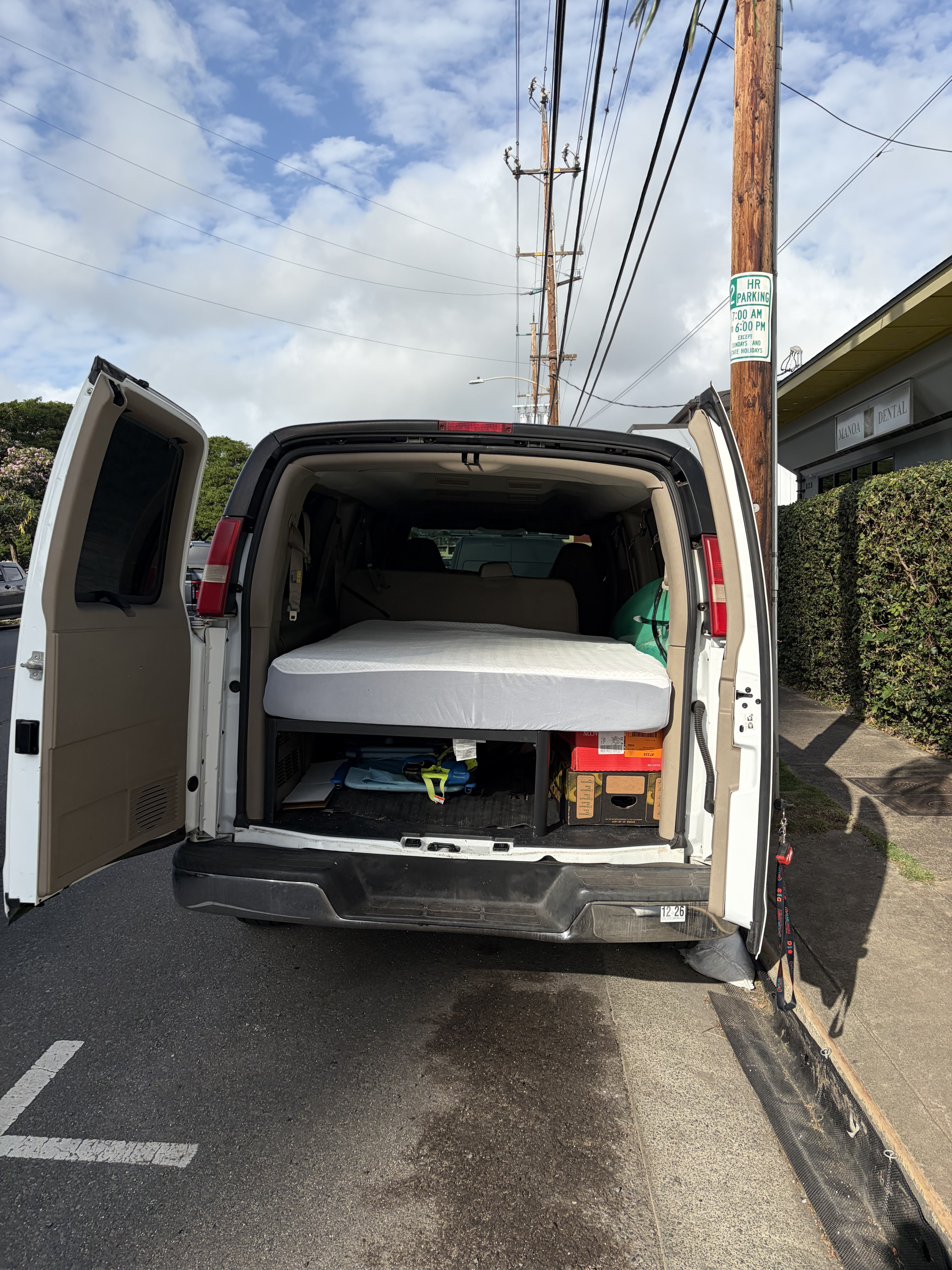 A white van, possibly an rv rental, is seen with its back doors open, revealing a mattress for sleeping, parked by a "2 HR PARKING" sign.. Chevrolet Chevrolet Express 3500 Extended 2009