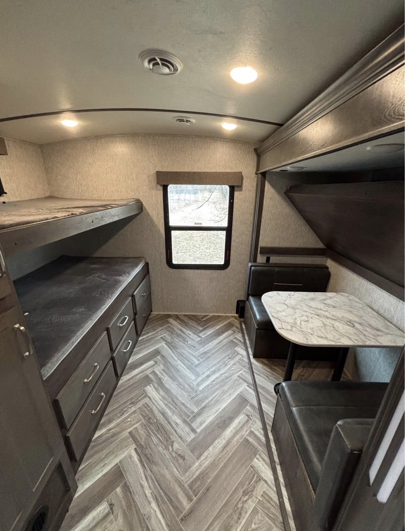 RV rental interior: bunk beds on left, a dinette with marble-patterned table on right, and stylish herringbone flooring.. Astoria Astoria Trailer 2022