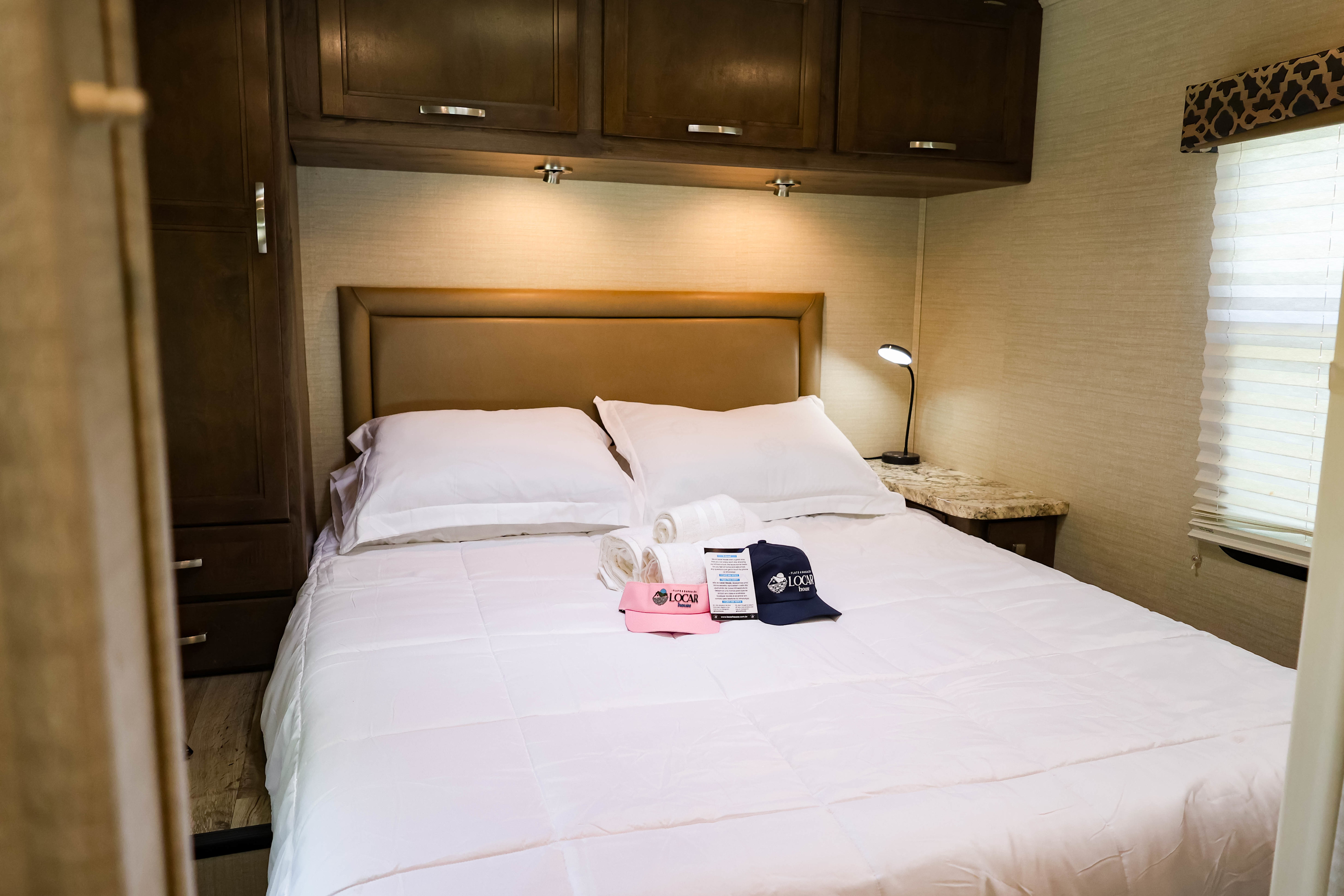 Cozy RV rental bedroom with comfortable bed, overhead storage, and bedside lamp. Includes "LOCAR house" branded items.. Adventurer Jayco Redhawk 29XK ano 2019 2019