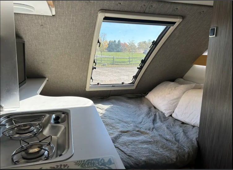 Enjoy the compact comfort of this RV rental, featuring a cozy bed, scenic window view, and a built-in kitchen stove.. nuCamp T@B 2020
