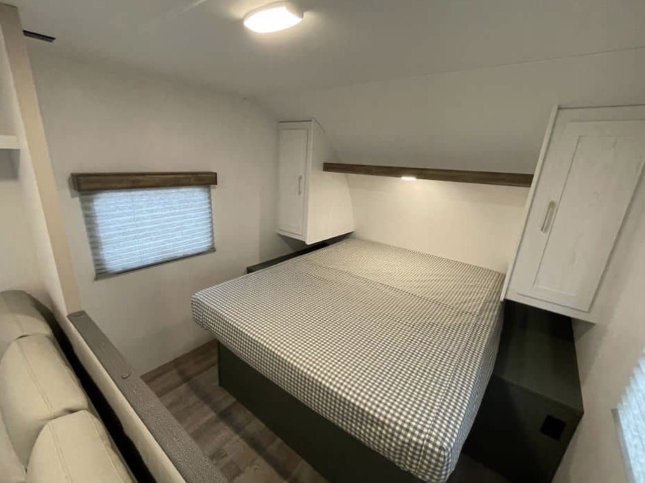 Cozy RV rental bedroom with a checkered bed, a window with blinds, and convenient overhead storage.. Heartland RVs Eddie Bauer 2024