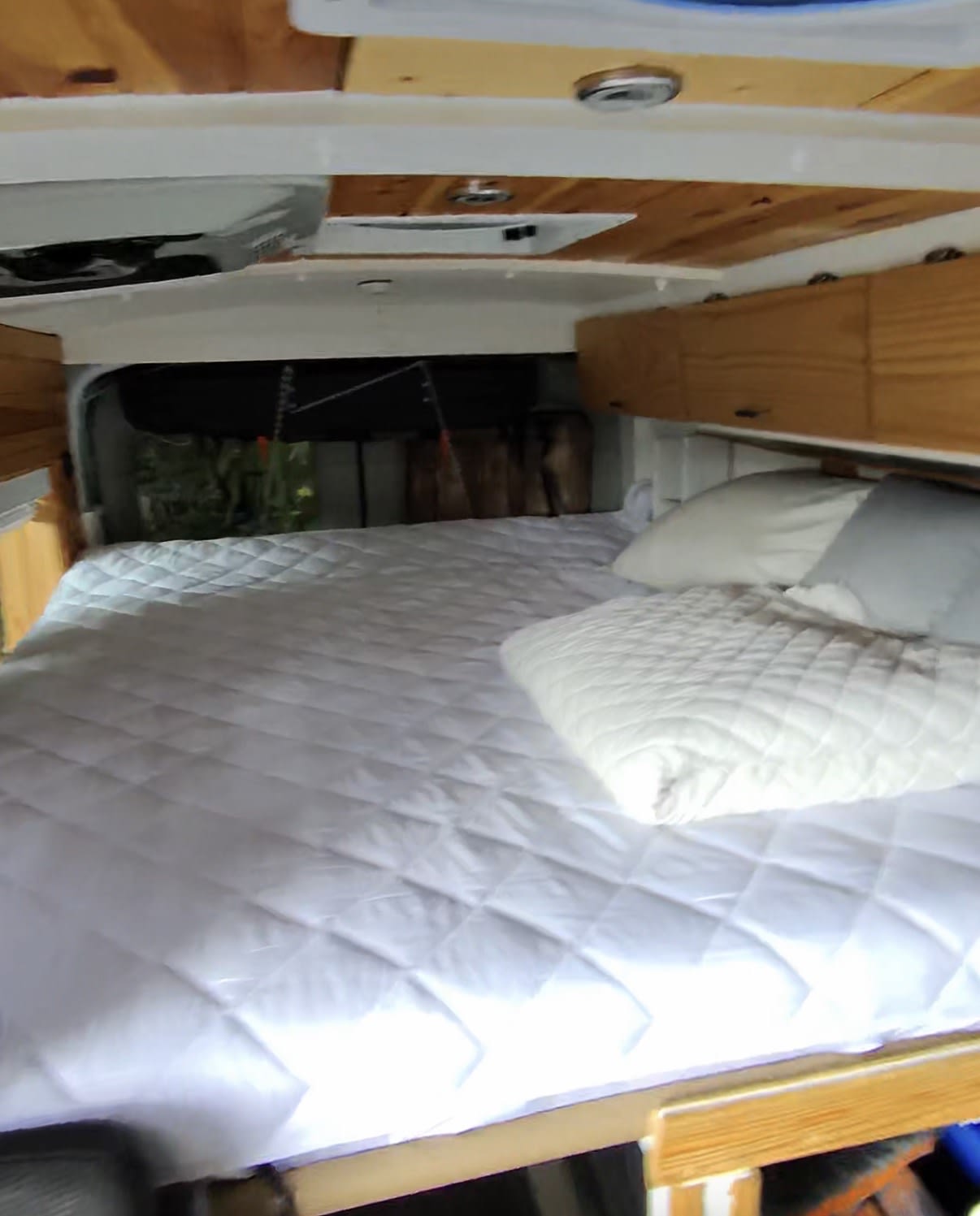 Cozy bed in an RV rental with wooden interior and overhead cabinets. Ready for a comfortable road trip.. Ford Transit 2017