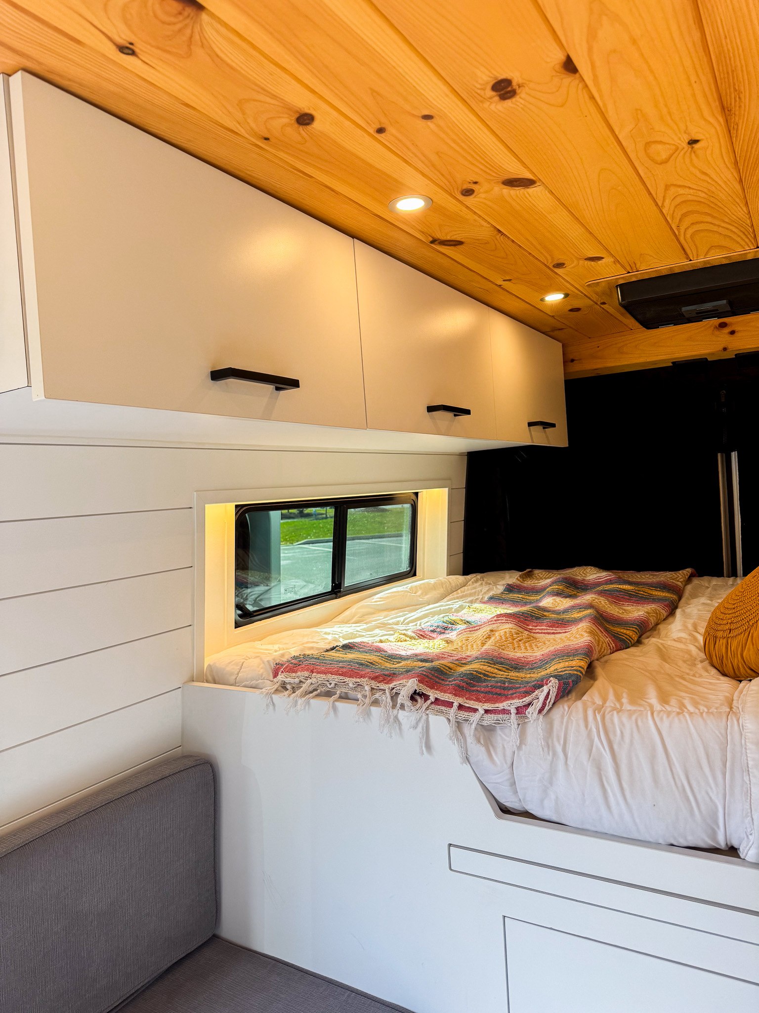 Modern RV rental van interior features a comfy bed, window nook, wood ceiling, and ample storage.. Ram Promaster 2022